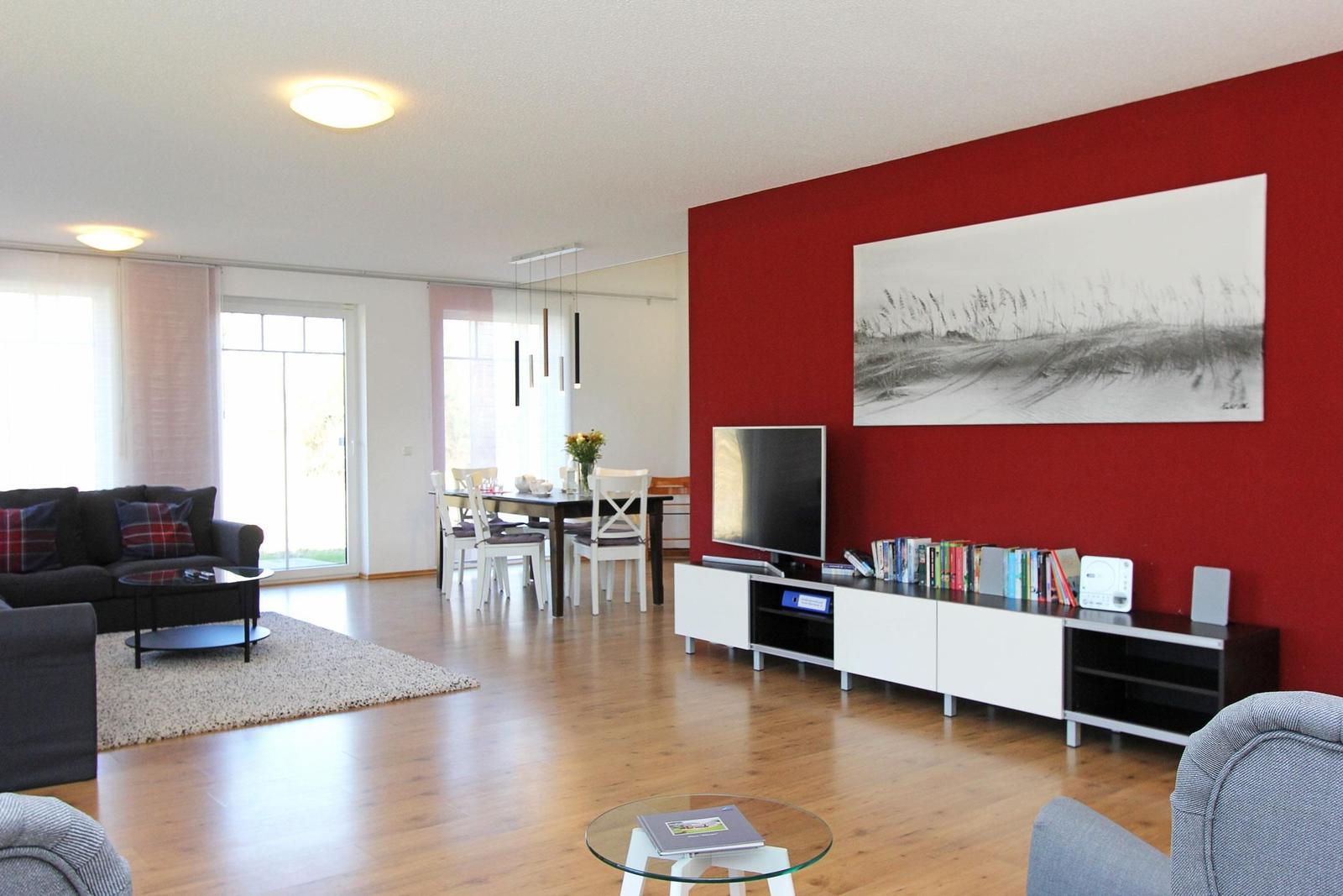 Wohn- und Essbereich mit roter Wand, TV, Sofa und Esstisch.