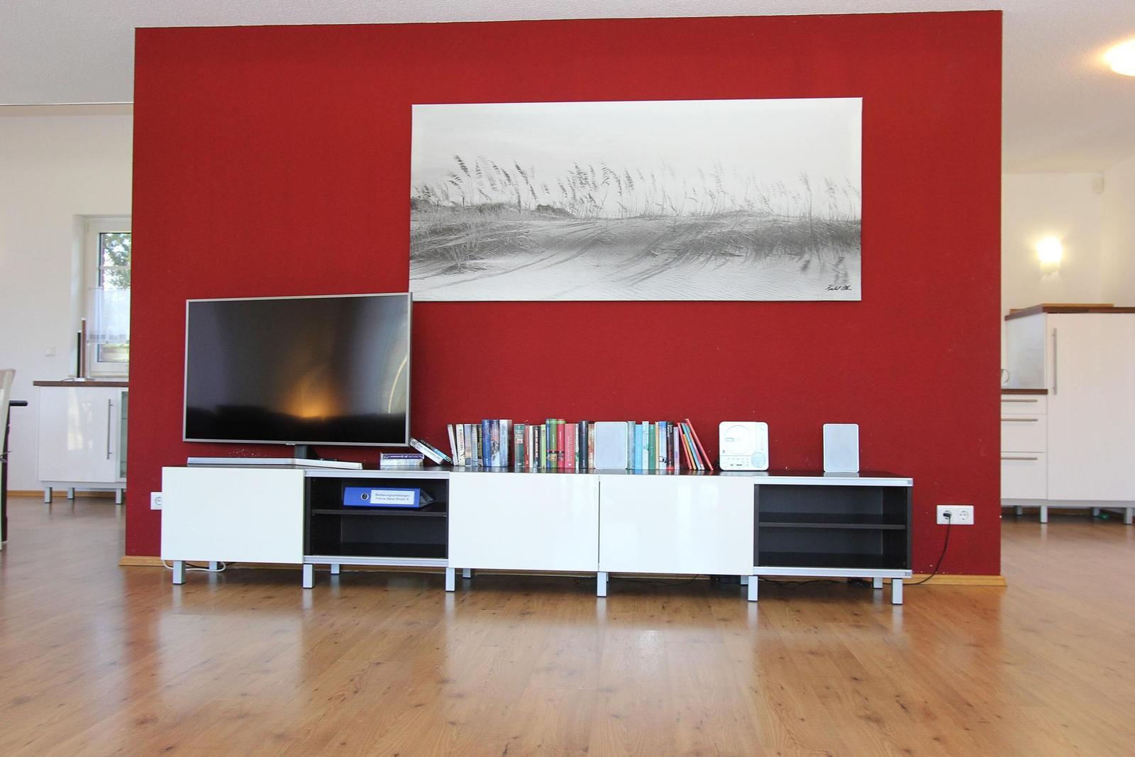 Roter Wandbereich mit Fernseher und Kunstwerk über einem weißen Sideboard.