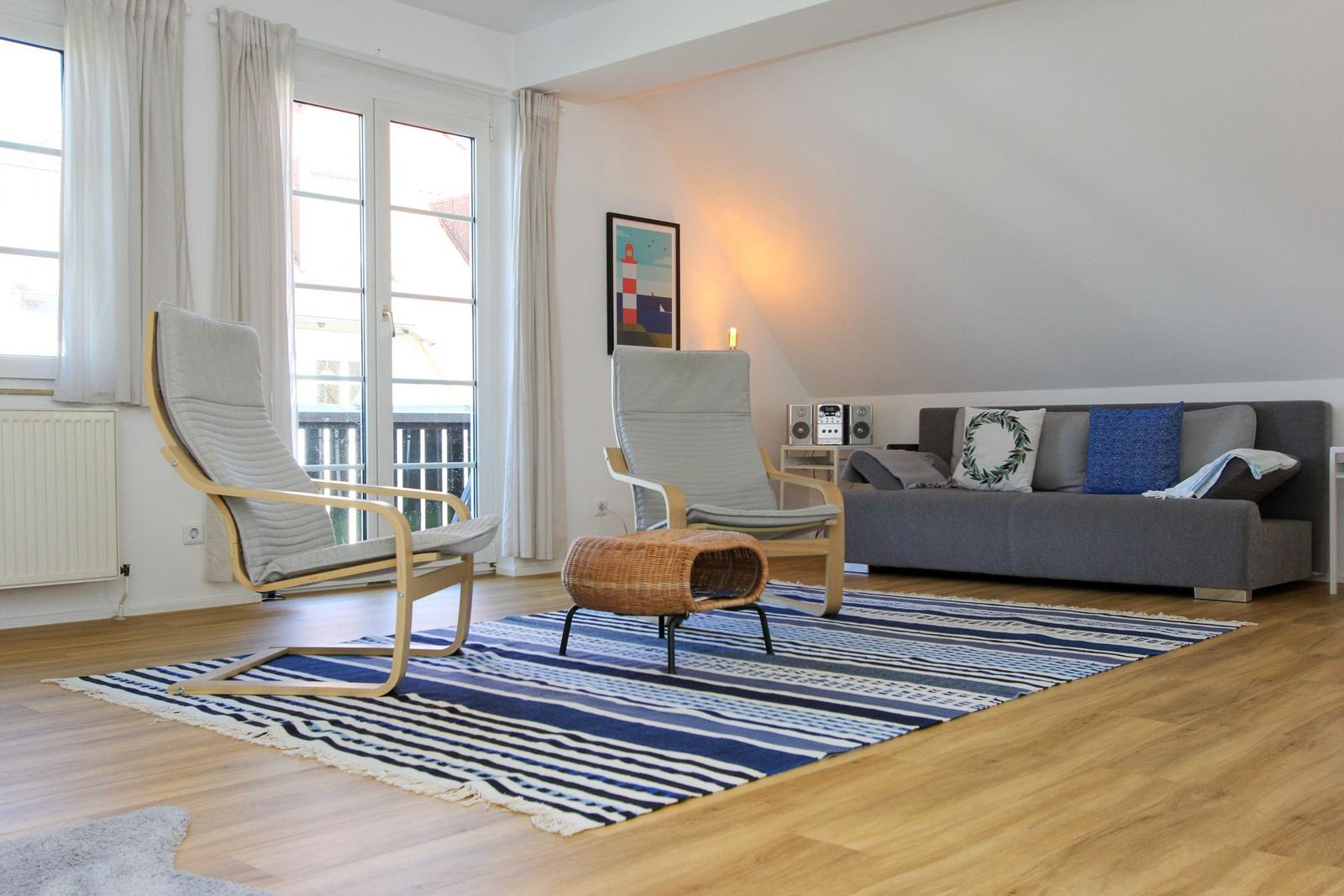 Wohnzimmer mit Sofa, zwei Sesseln und blau-weißem Teppich auf Holzboden.