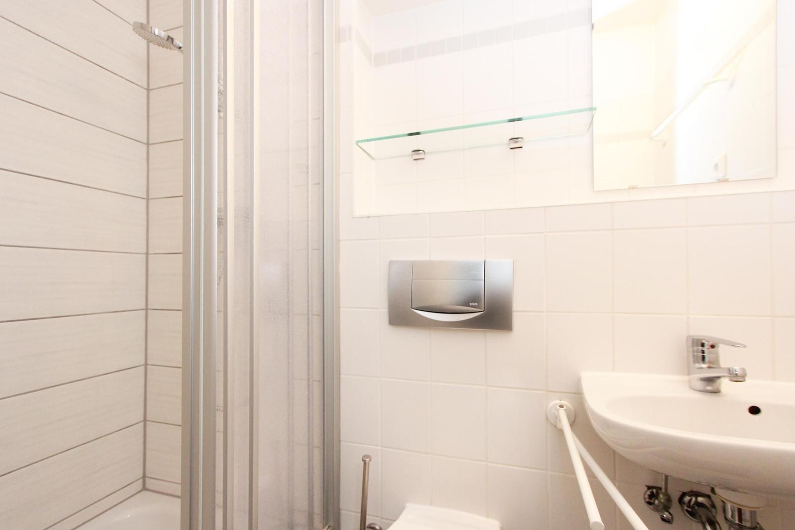 Badezimmer mit Dusche, Waschbecken und Spiegel.