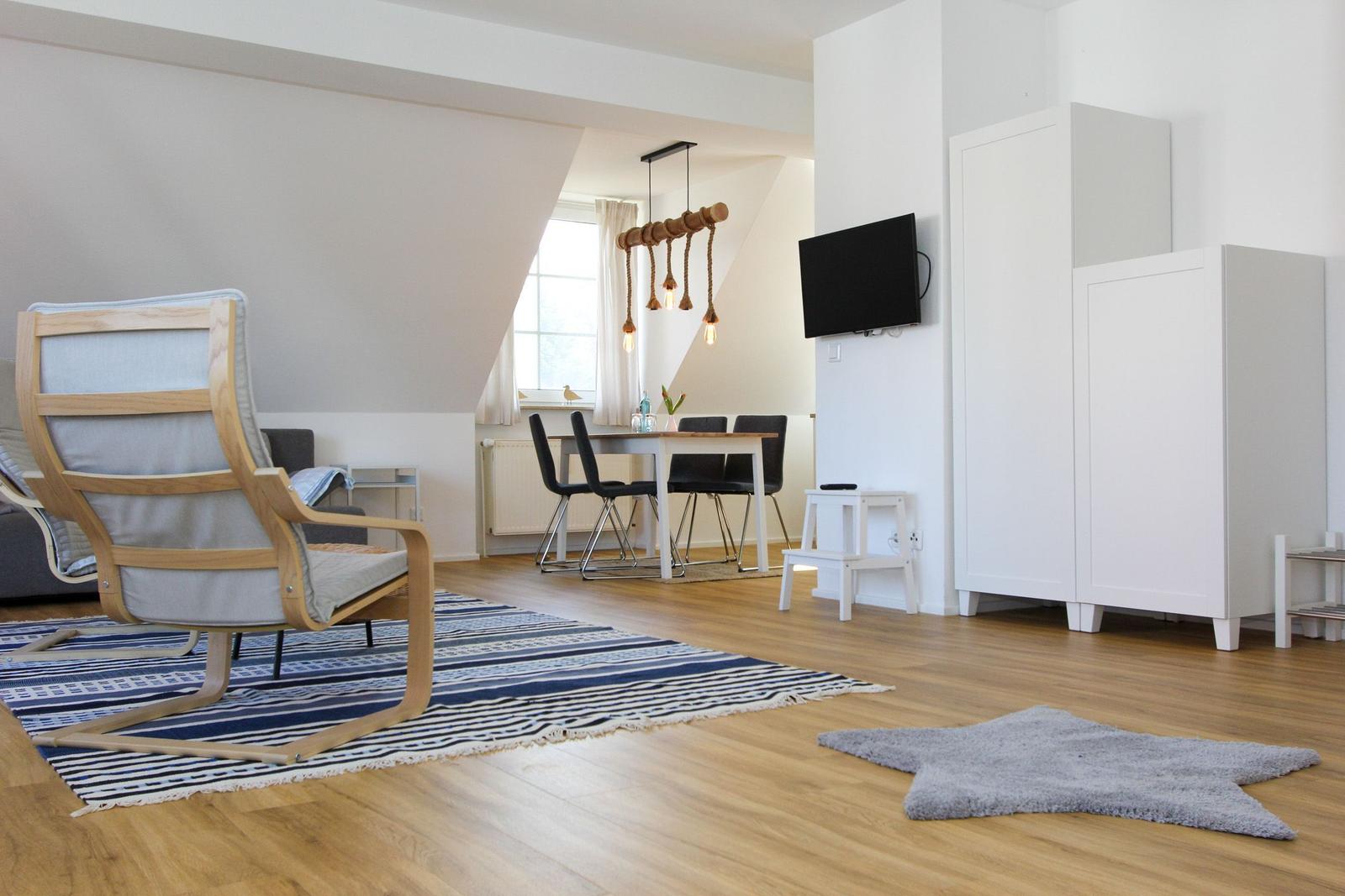 Wohn- und Essbereich mit Holzboden, TV, Schrank und Sitzgelegenheiten.