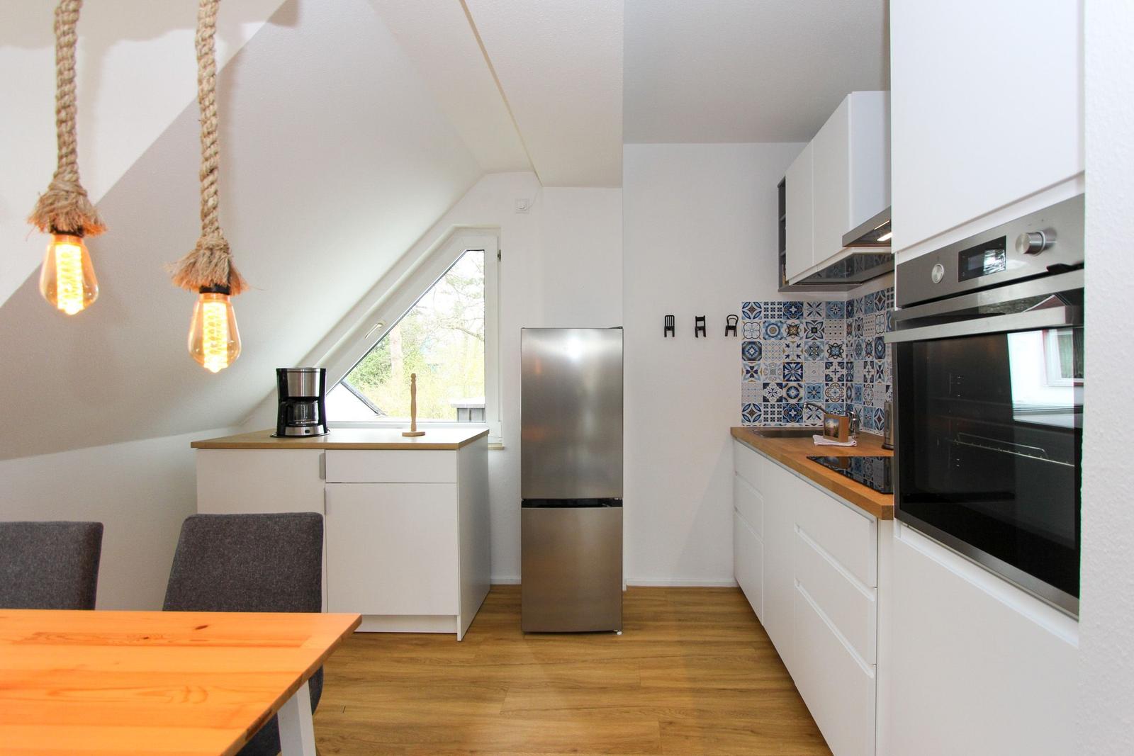 Küche mit Holzoberflächen, Kühlschrank und Ofen. Dachfenster und hängende Lampen.