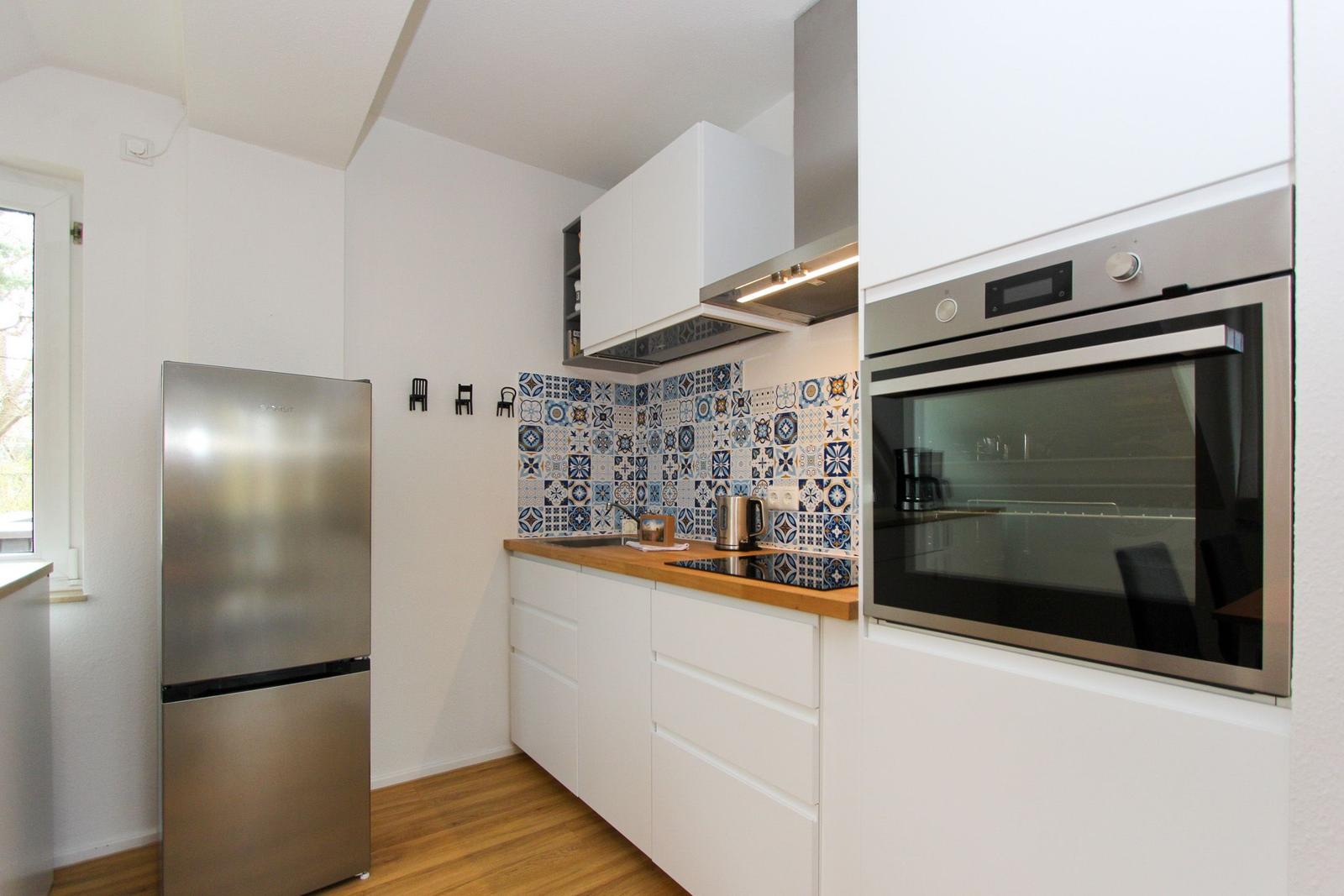 Küche mit weißer Einbauküche, Edelstahl-Kühlschrank und integriertem Backofen.