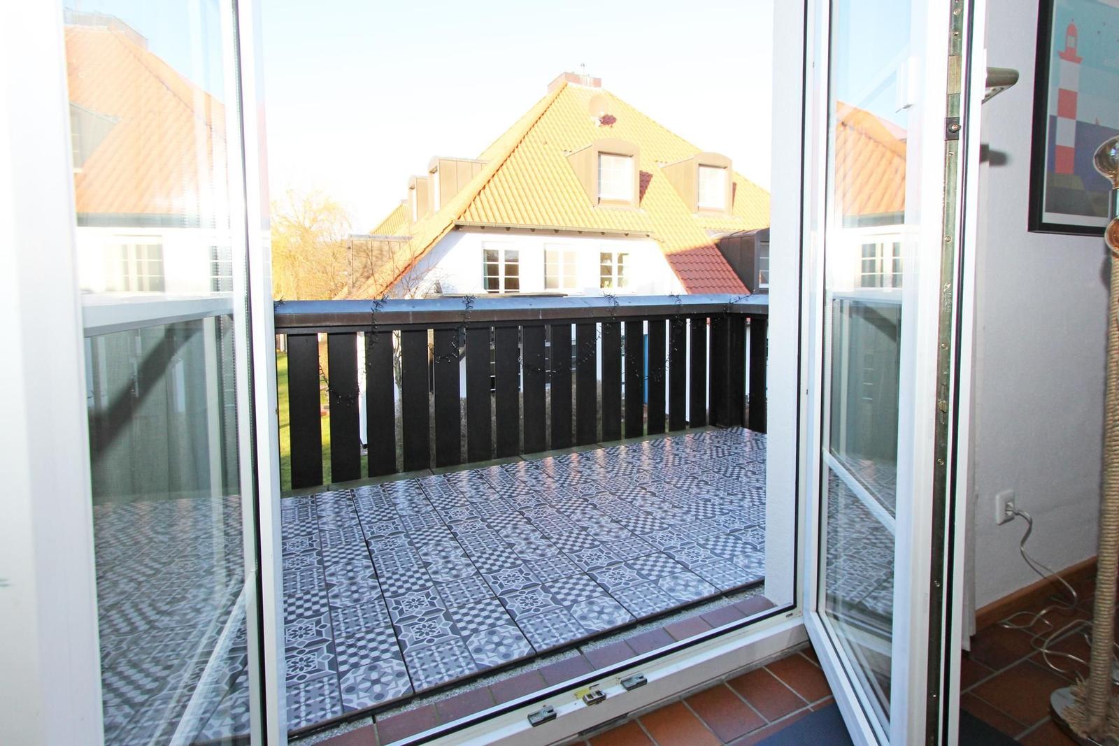 Terrasse mit schwarz-weißen Fliesen und Holzgeländer. Blick auf ein Haus mit gelbem Dach.