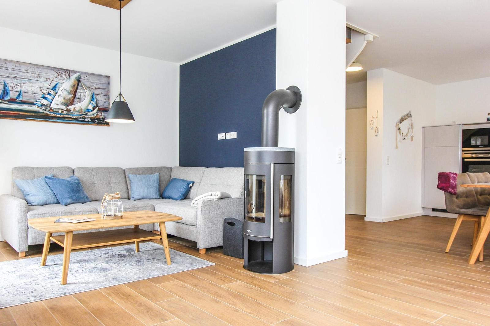 Wohnzimmer mit Sofa, Couchtisch und Kaminofen. Wand mit Segelyacht-Bild.