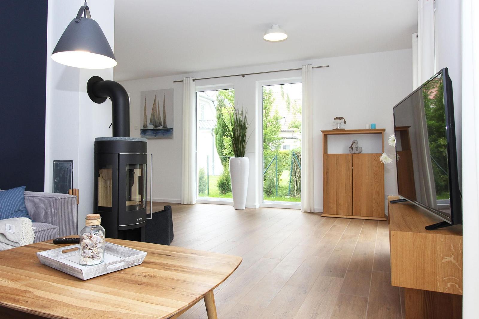 Wohnzimmer mit Holzboden, Kaminofen, TV und Blick auf Garten.