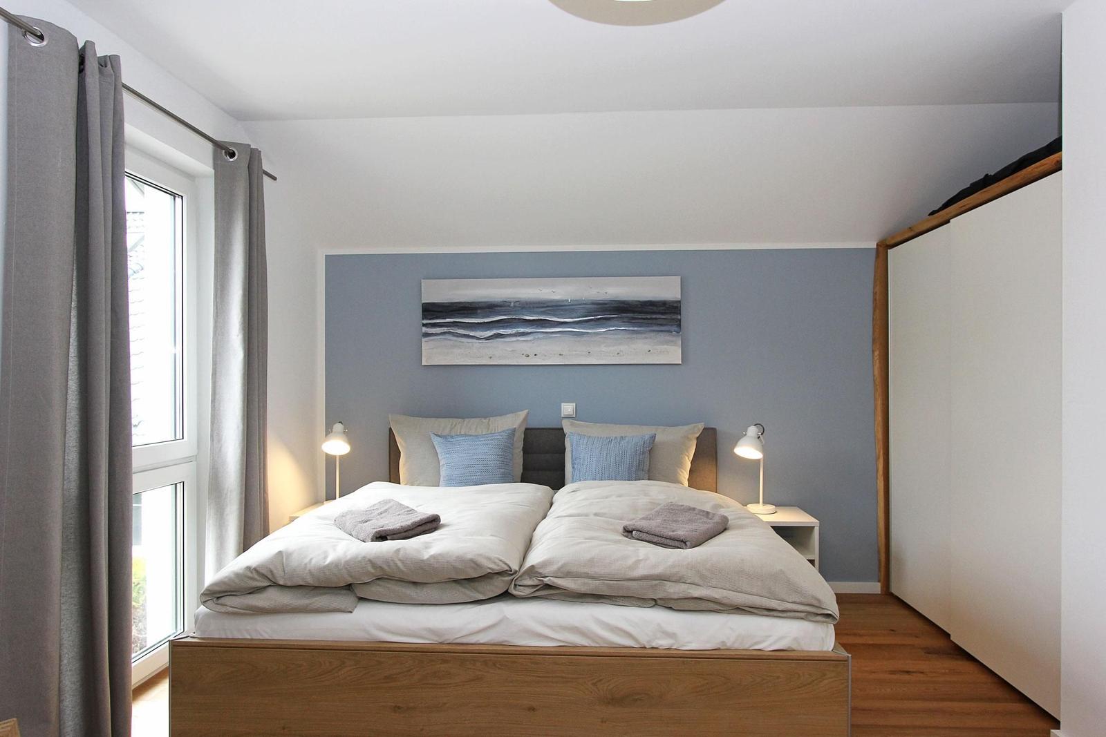 Schlafzimmer mit Doppelbett, Wandbild und zwei Nachttischen mit Lampen.