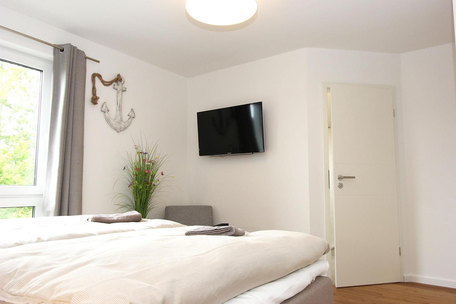 Schlafzimmer mit Bett, Fernseher und Fenster mit Blick auf Grün.