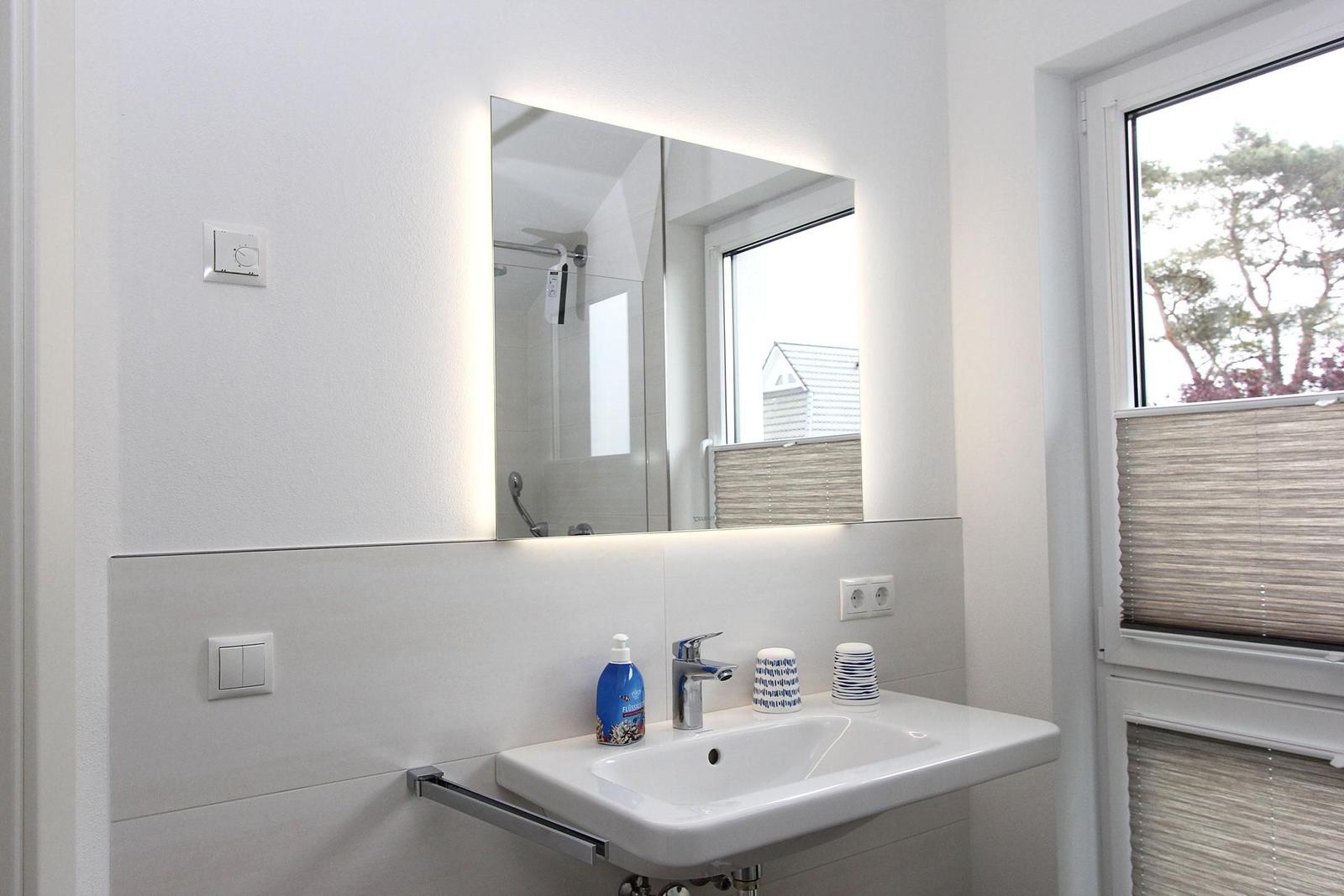 Bad mit Waschbecken, beleuchtetem Spiegel und Fenster mit Jalousie.