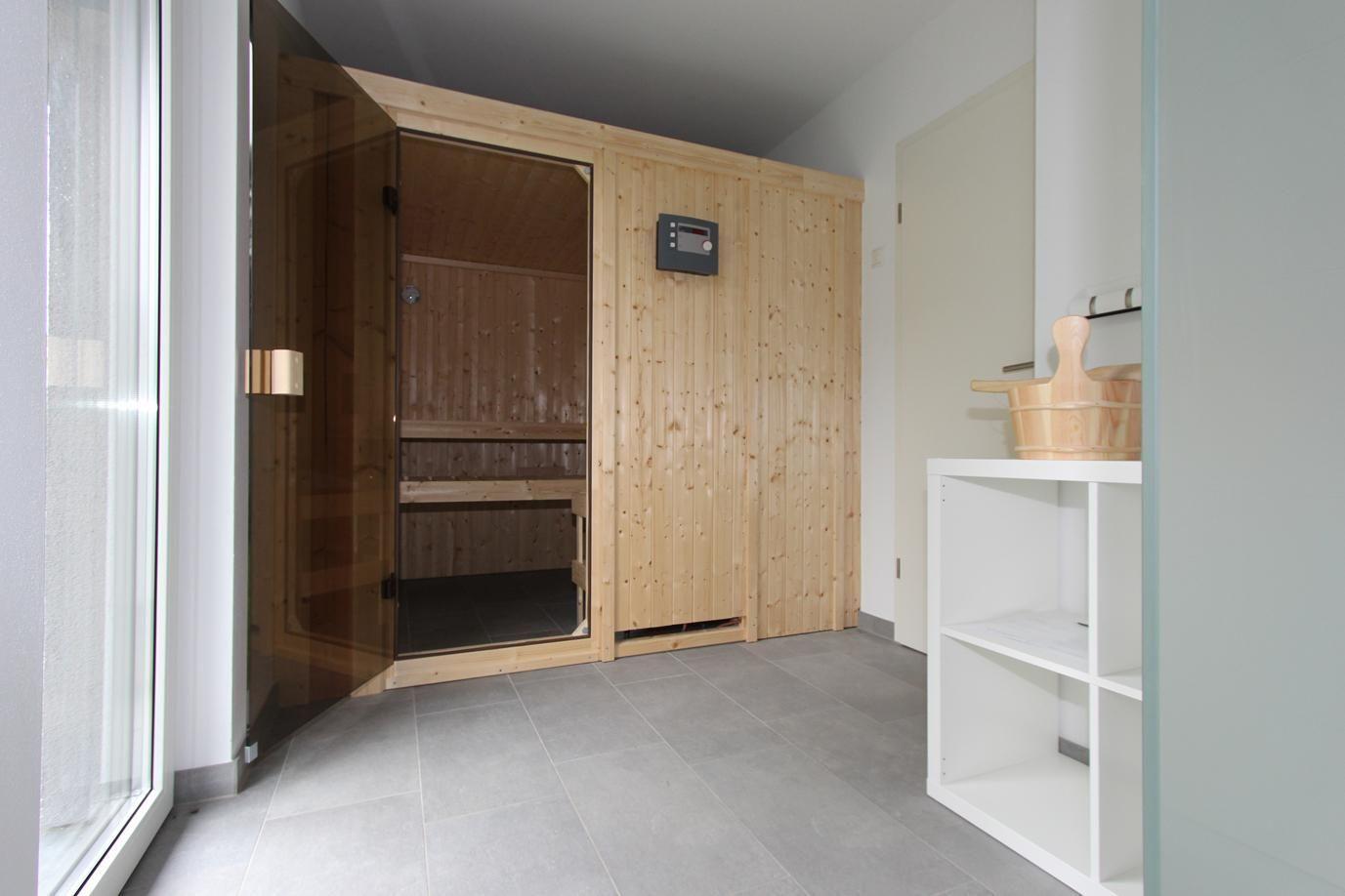 Sauna mit Holzverkleidung und Sitzbänken. Neben einem weißen Regal mit Holzschale.