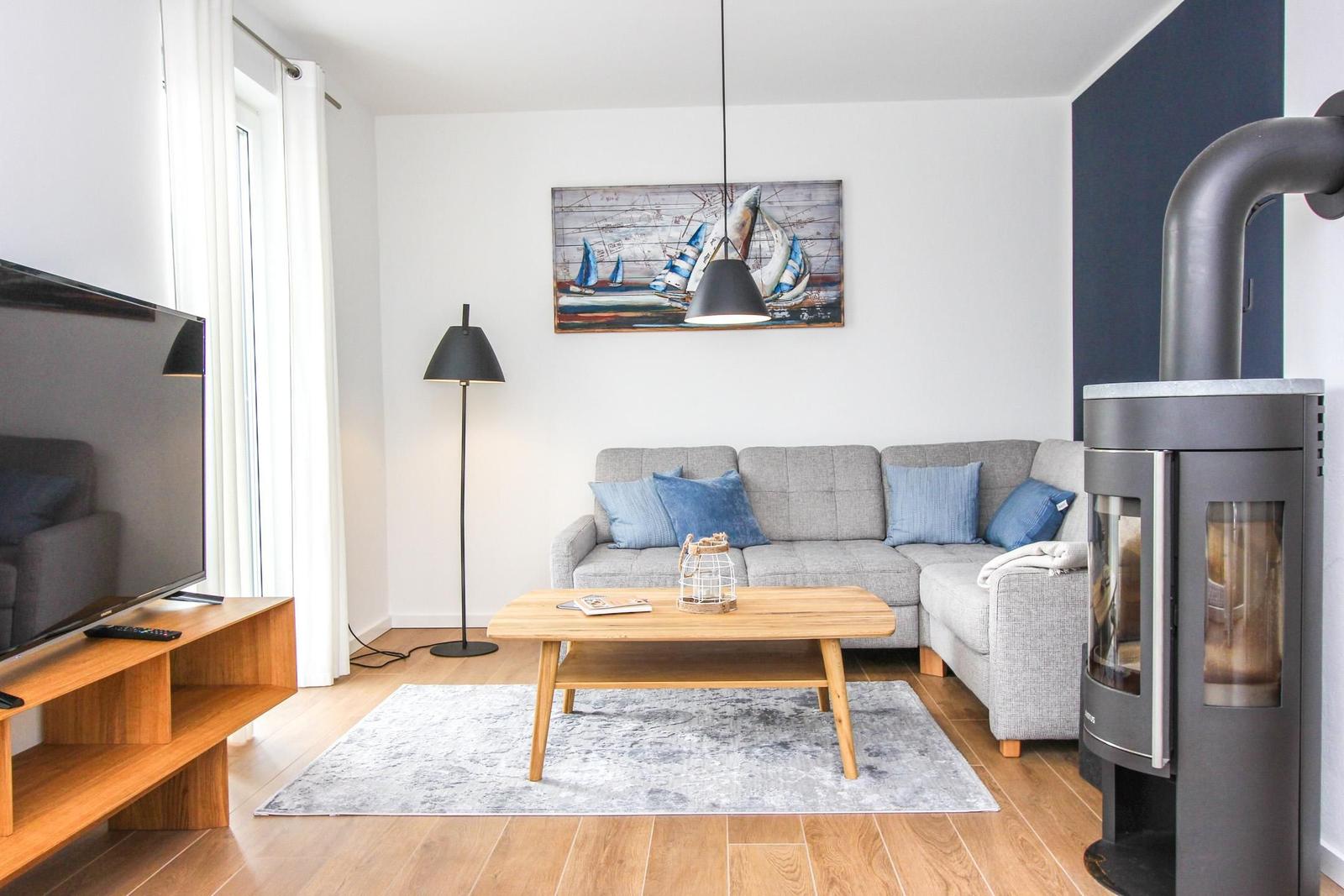 Wohnzimmer mit Sofa, Couchtisch, Fernseher und Kaminofen.