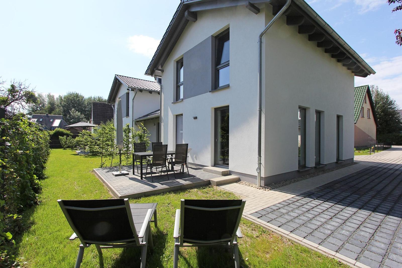 Moderne Villa mit Terrasse, Garten und Liegestühlen. Außenbereich mit Tisch und Stühlen.