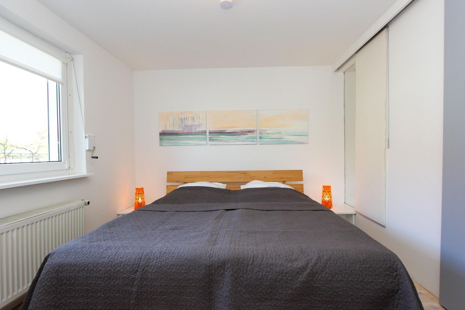 Schlafzimmer mit Bett, Fenster, Schrank und Wandbildern.