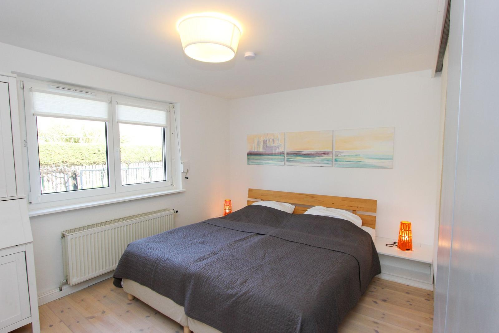 Schlafzimmer mit Doppelbett, Fenster und Wandbildern.