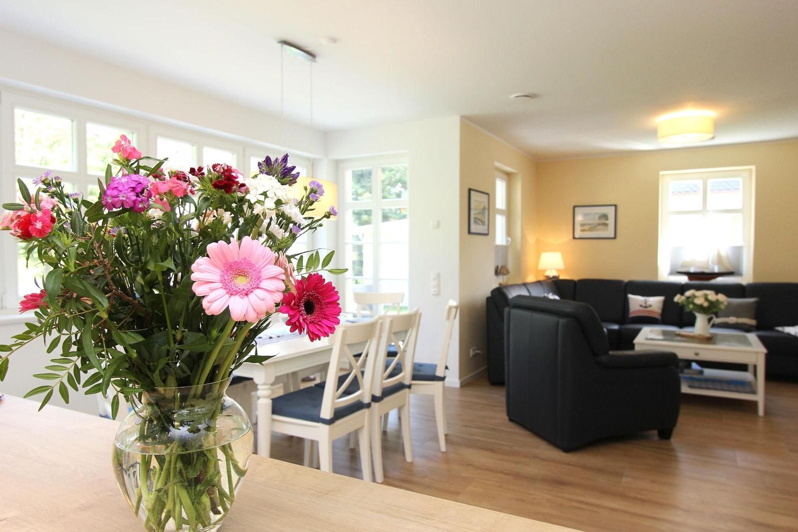Ein Essbereich mit Blumen und ein Wohnzimmer mit schwarzer Couch.