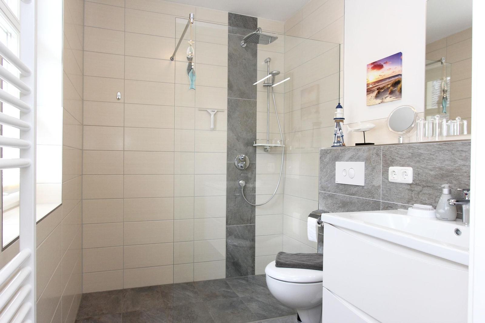 Bad mit Dusche, WC und Waschbecken. Fliesenwand und graue Bodenfliesen.