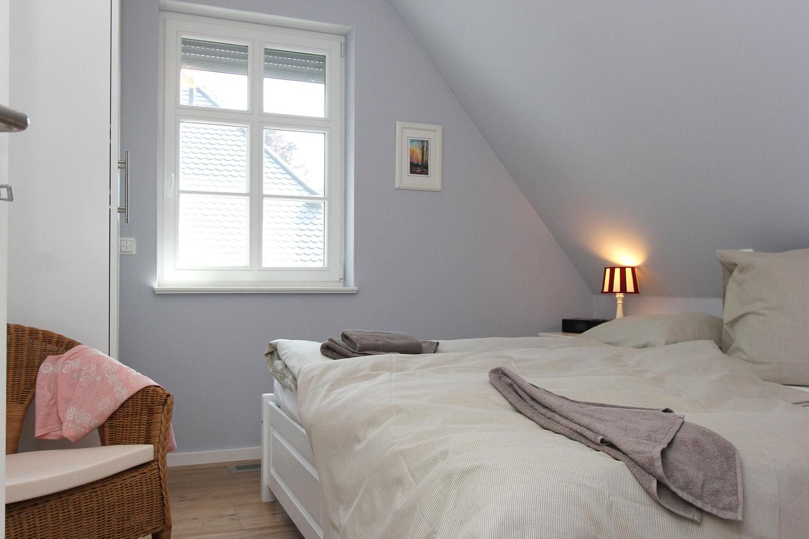 Schlafzimmer mit Dachschräge, Fenster und Bett. Neben dem Bett steht eine Lampe.