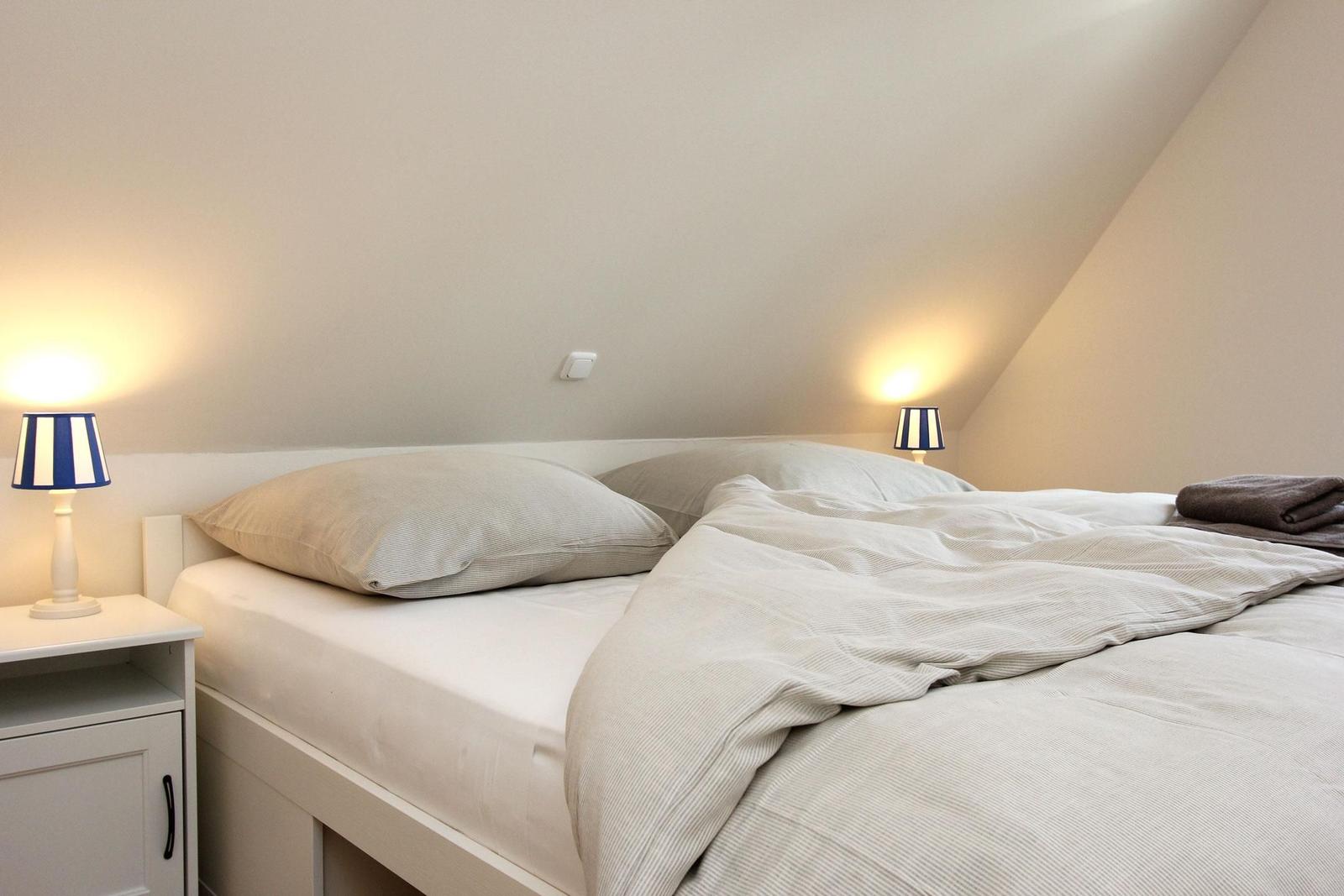 Schlafzimmer mit Bett, zwei Nachttischen und Lampen unter schrägem Dach