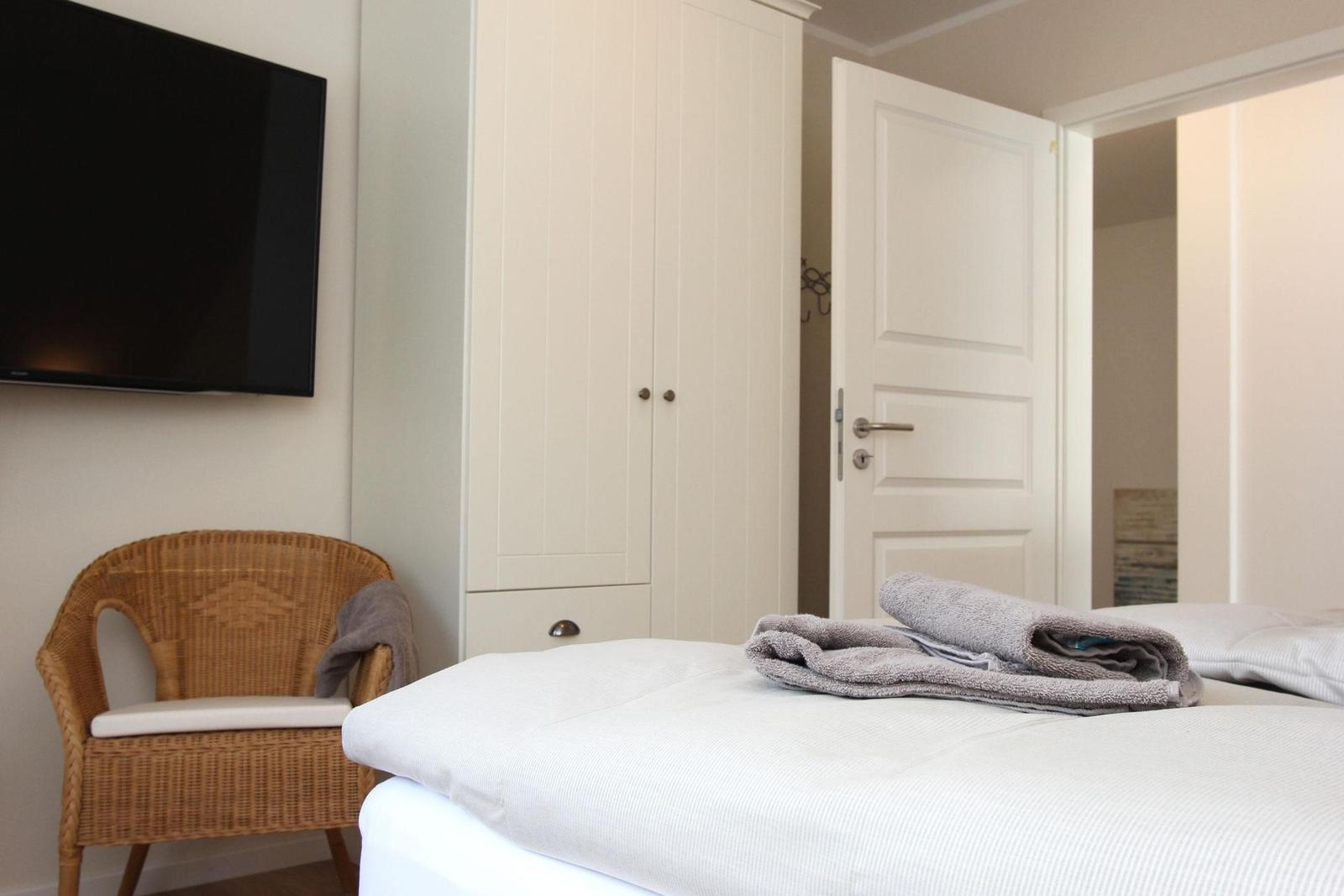 Schlafzimmer mit Bett, Kleiderschrank, TV und Stuhl.