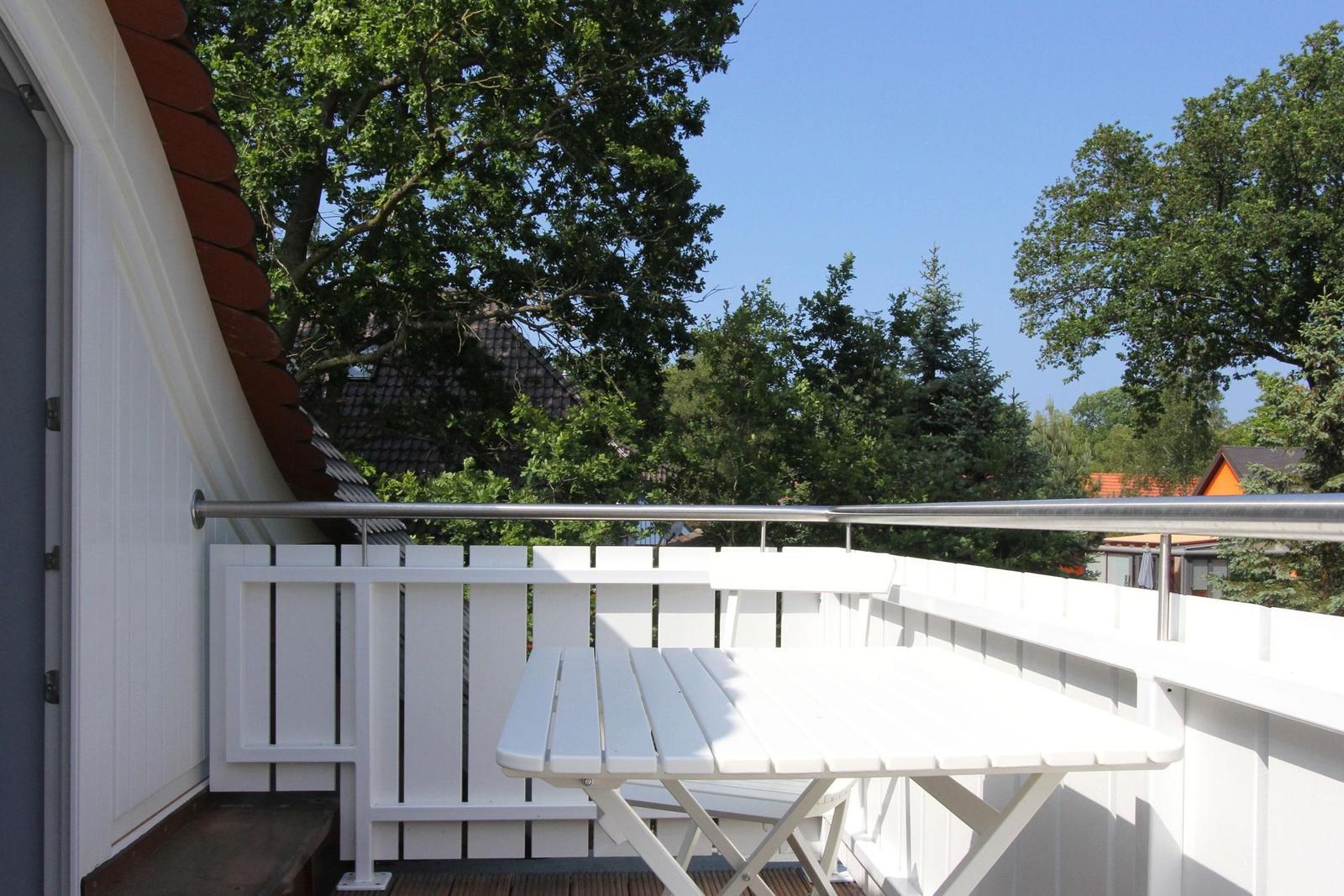 Terrasse mit weißem Tisch und Bänken, umgeben von Bäumen und einem klaren Himmel.