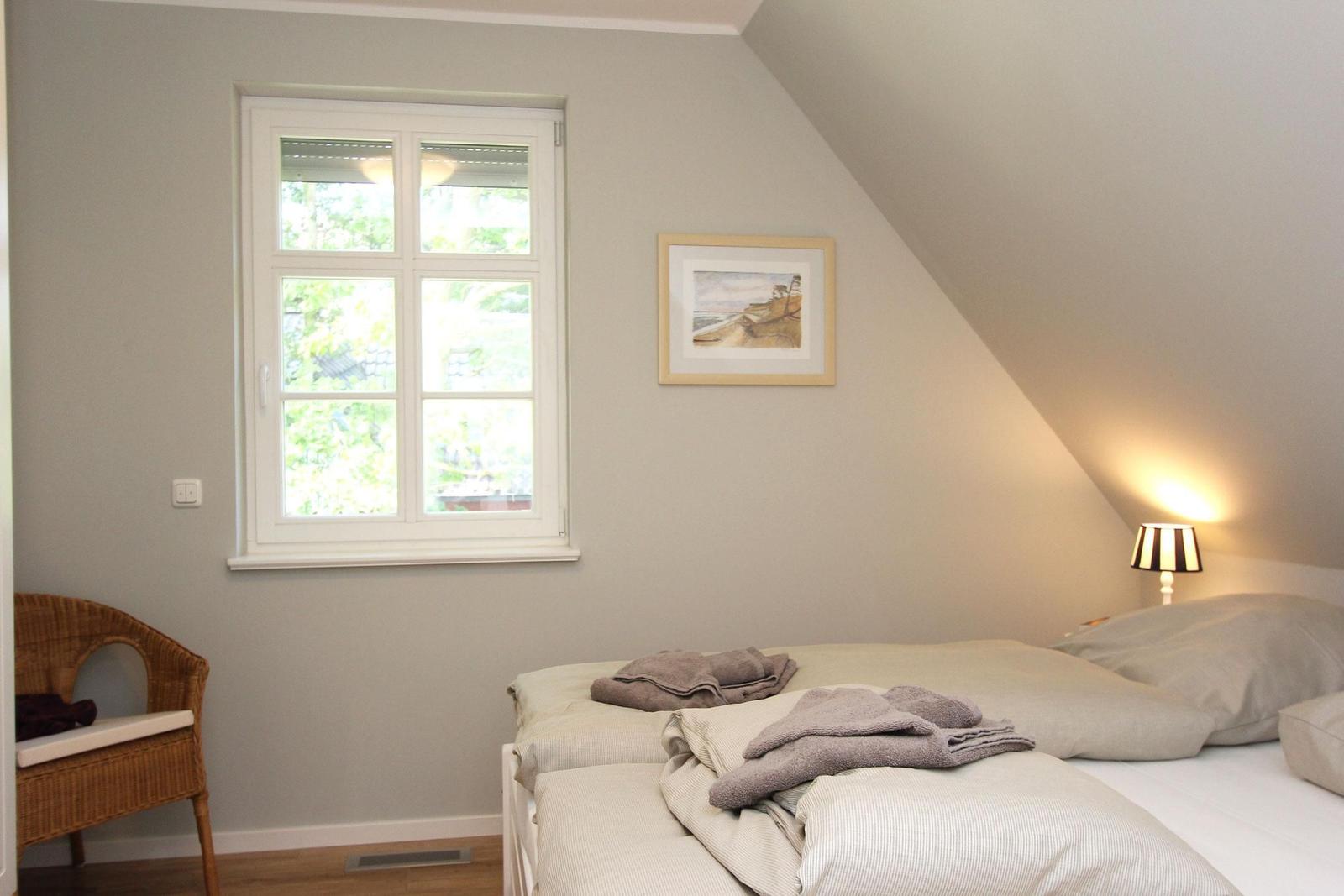Schlafzimmer mit Dachschräge, Fenster, Bett und Stuhl.