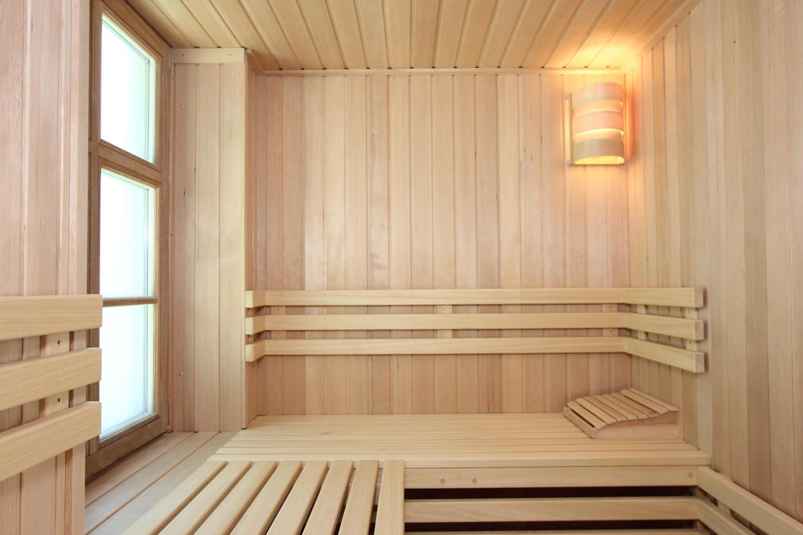 Holzsauna mit Sitzbänken und Fenster. Wandlampe an der Seite.