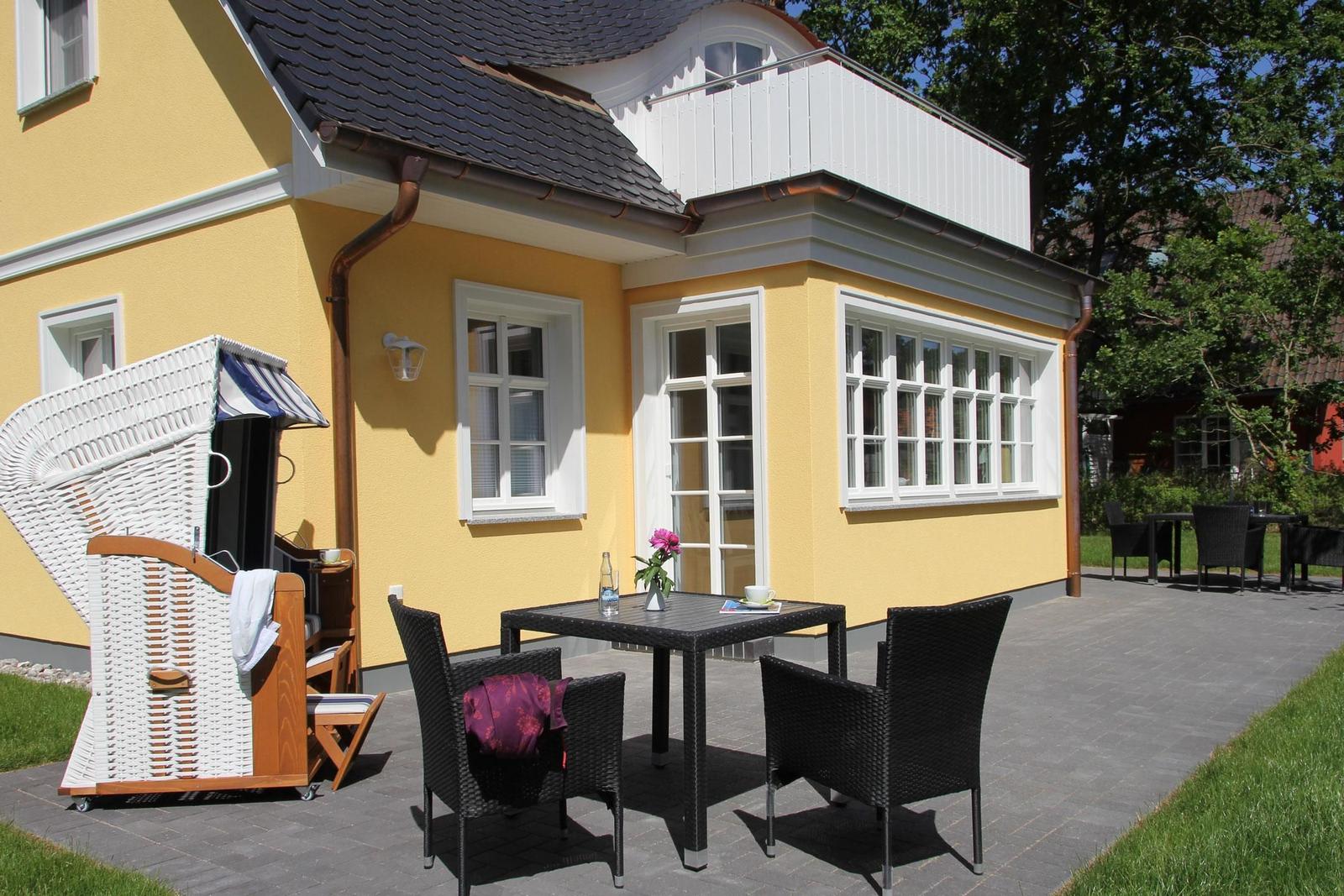 Außenbereich mit Tisch, Stühlen und Strandkorb vor gelbem Haus mit Balkon.