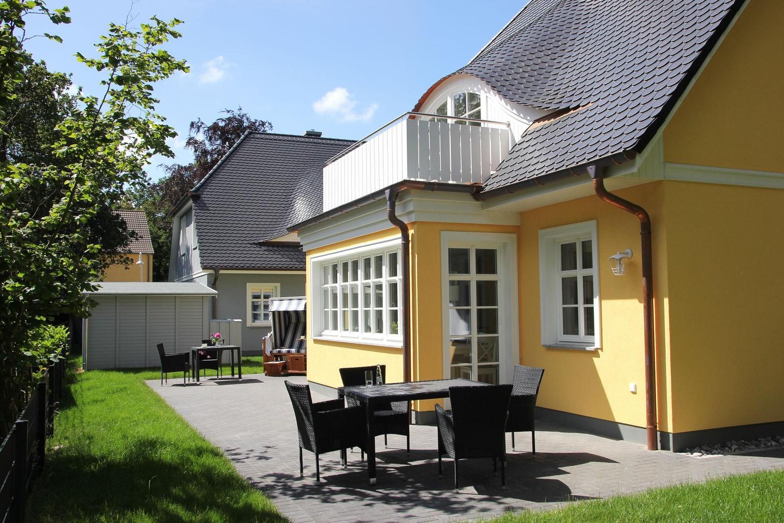 Gelbes Haus mit Balkon, Terrasse und Garten. Tisch und Stühle im Freien.