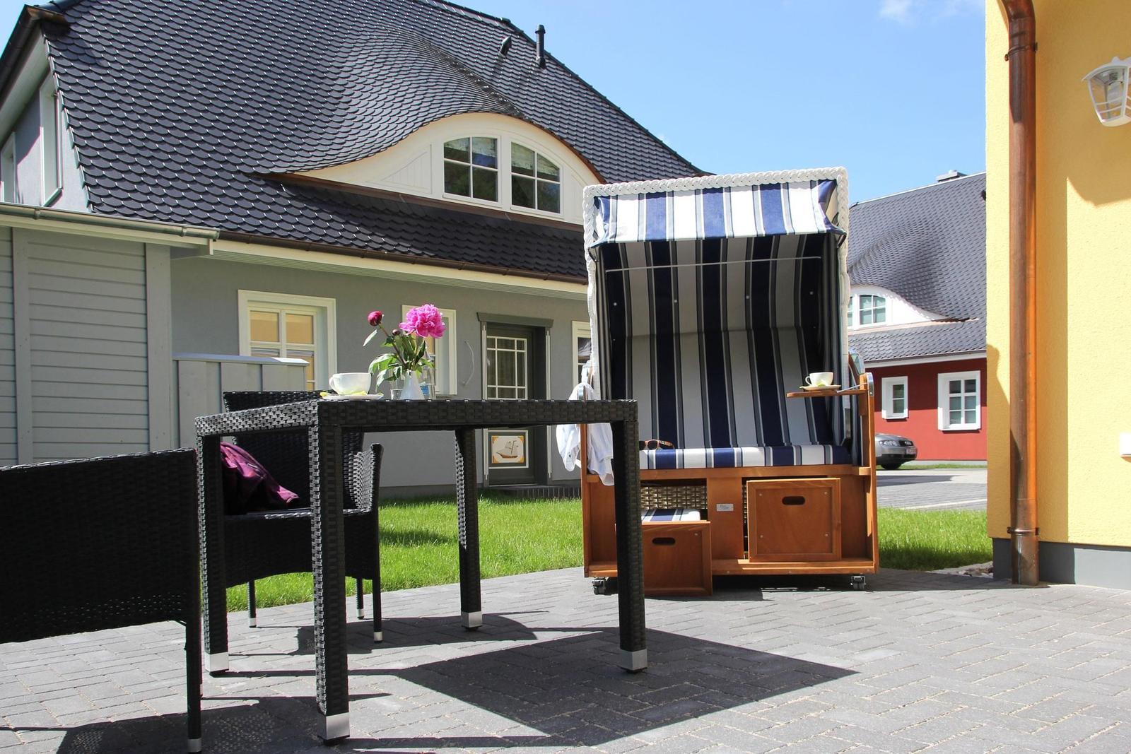 Terrasse mit Tisch, Stühlen und Strandkorb. Hintergrund: Haus mit Schieferdach.