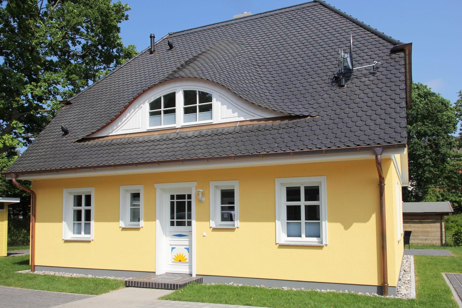 Ein gelbes Haus mit schwarzem Dach und weißen Fenstern. Vordere Tür mit Sonnenmotiv.