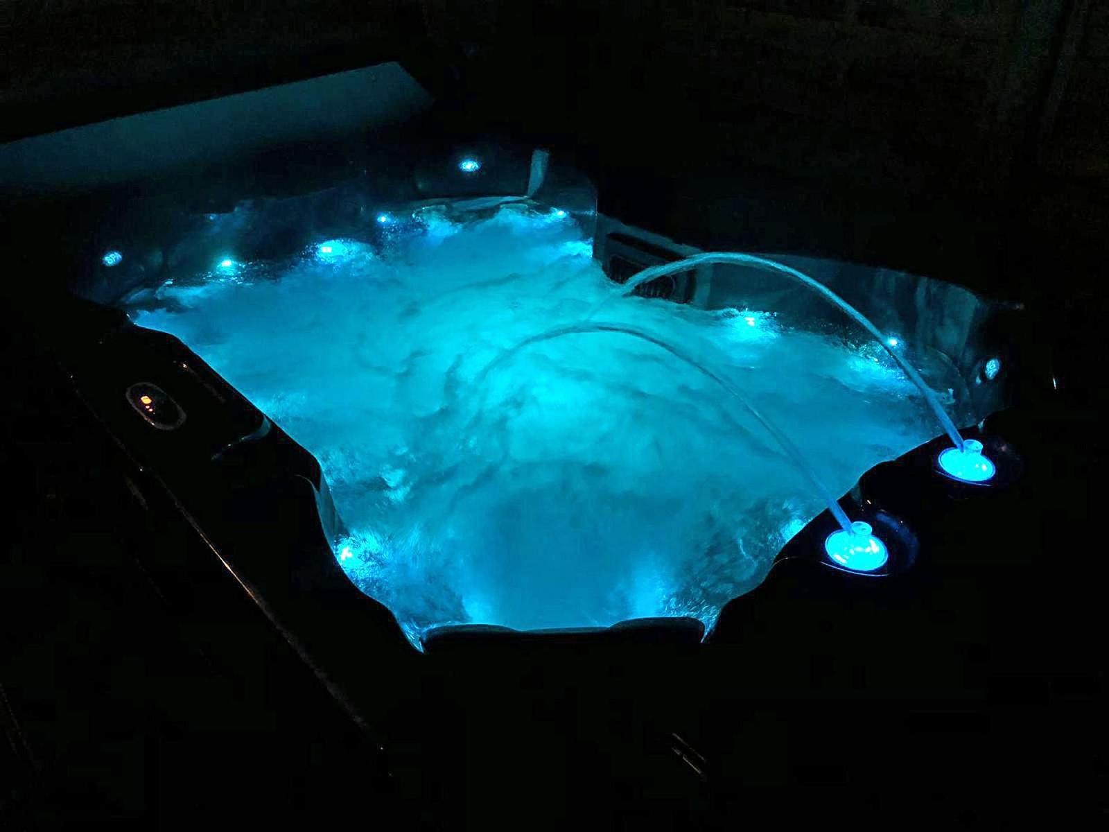 Ein Whirlpool mit blauer Beleuchtung und sprudelndem Wasser in der Dunkelheit.