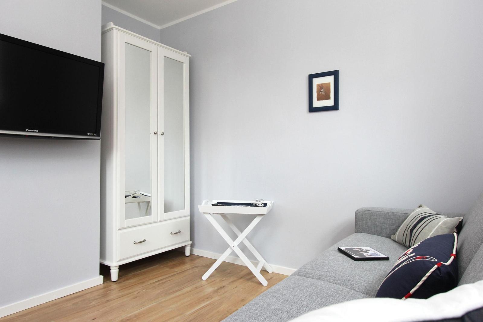 Wohnzimmer mit Sofa, Kleiderschrank und Fernseher an der Wand.