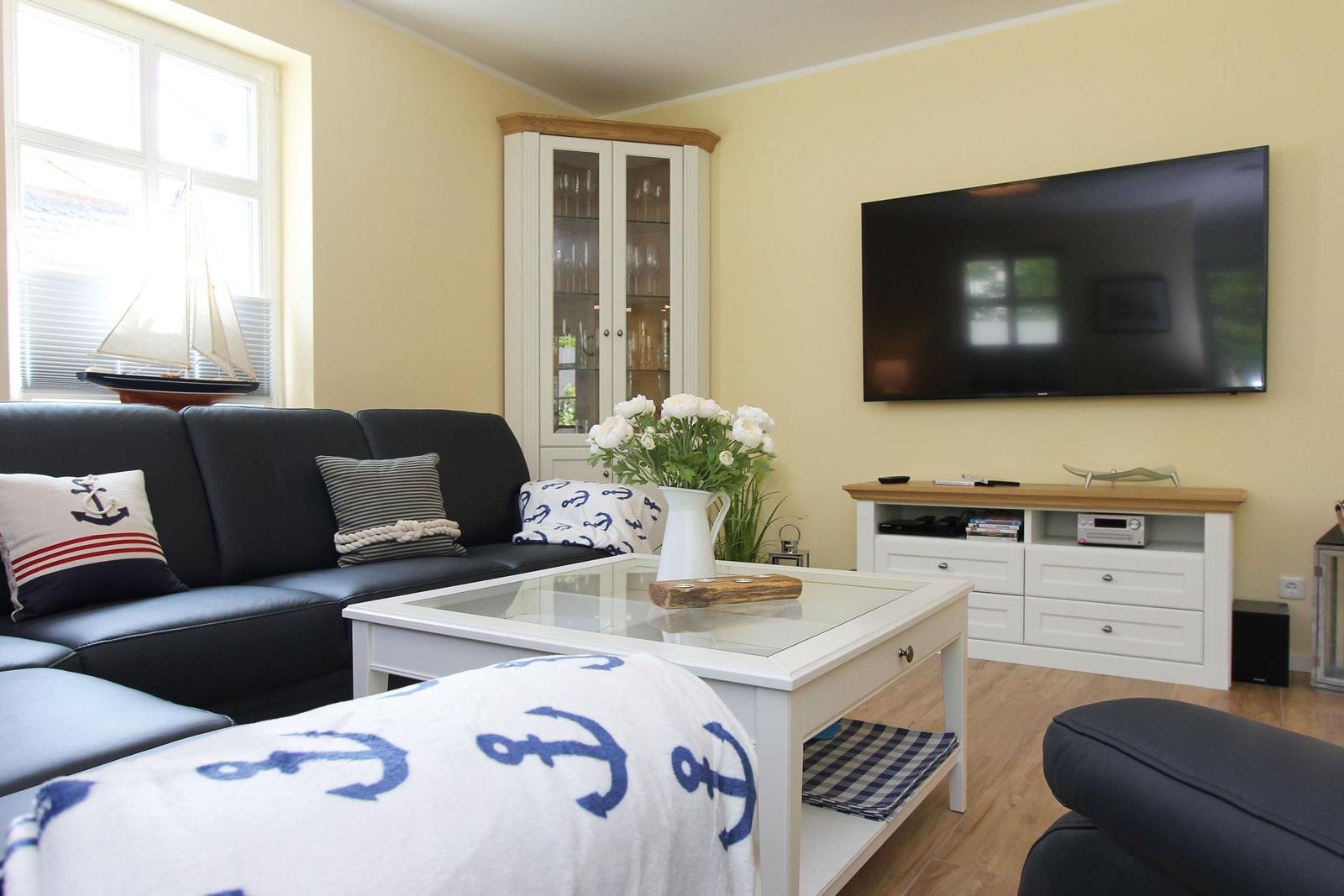 Wohnzimmer mit Sofa, Fernseher und Glaswand. Dekoration mit Ankern und Blumen.