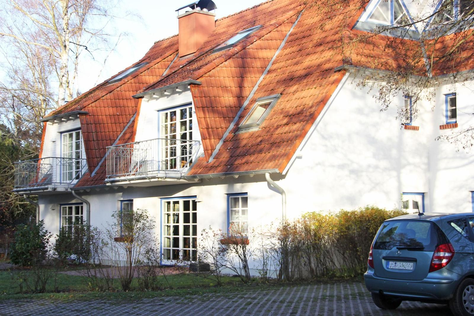 Ein weißes Haus mit rotem Dach, Balkon und Fenstern mit blauen Rahmen.