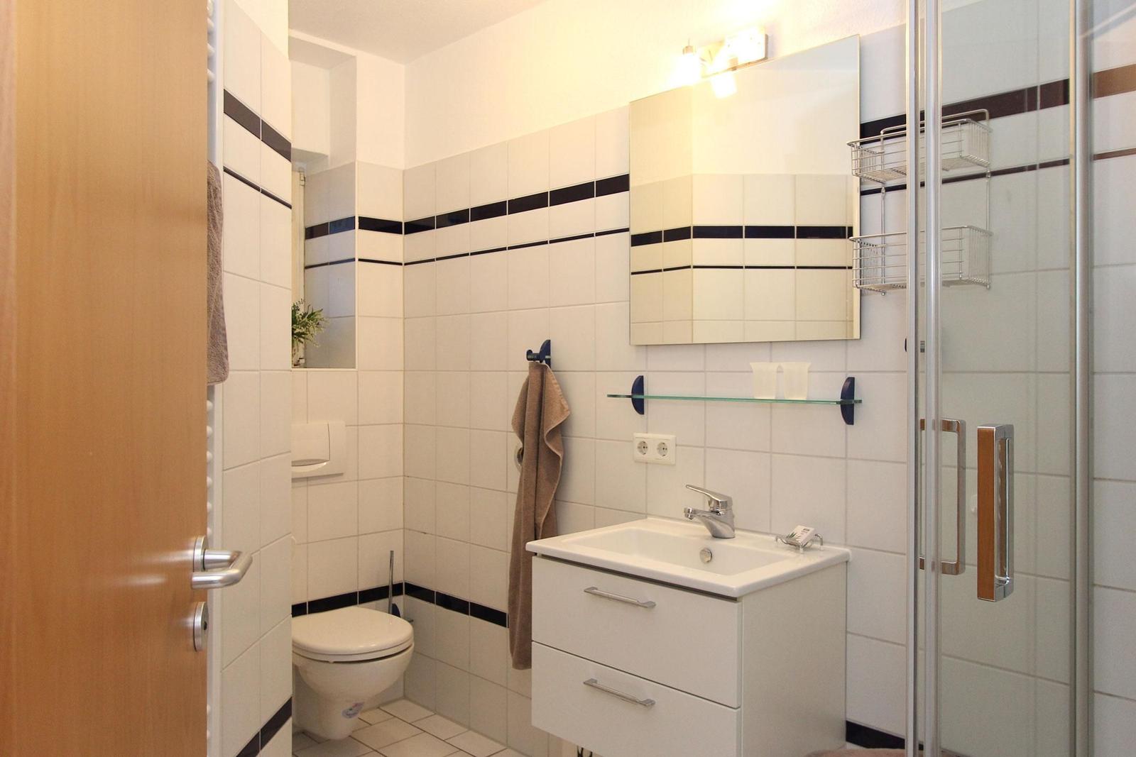 Badezimmer mit Dusche, Waschbecken und Toilette. Fliesen mit dunklen Streifen.