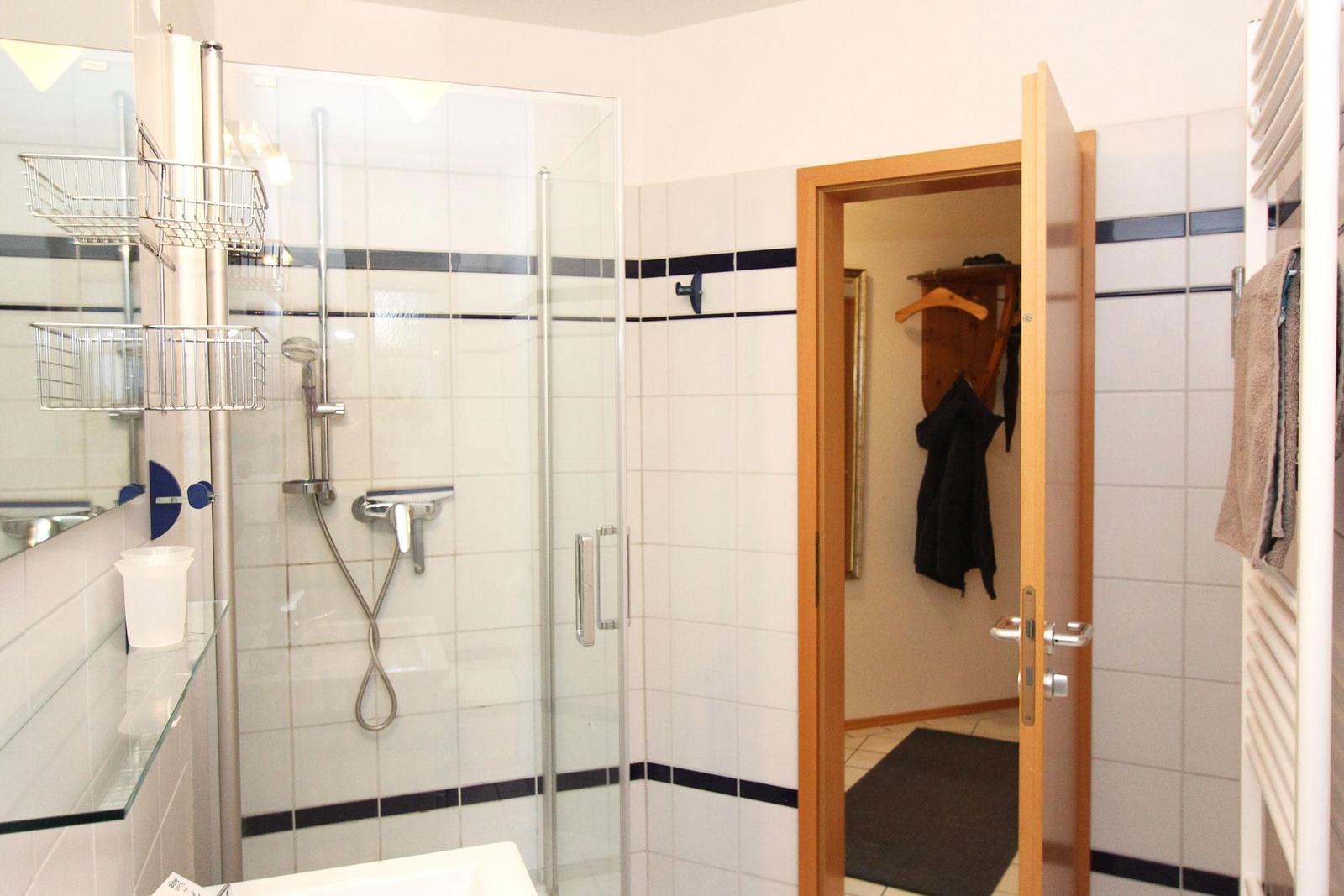 Badezimmer mit Dusche, Spiegelschrank und angrenzender Garderobe.