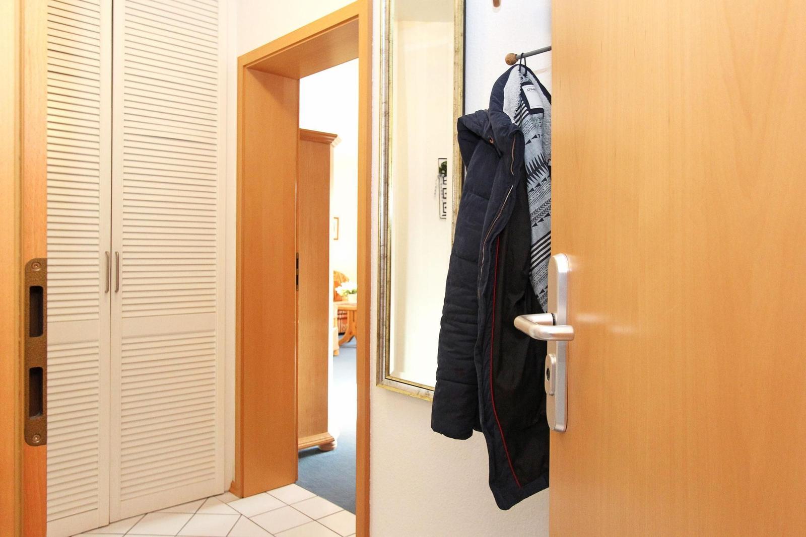 Eingangsbereich mit Kleiderhaken, Spiegel und Schrank. Tür zum Wohnzimmer sichtbar.