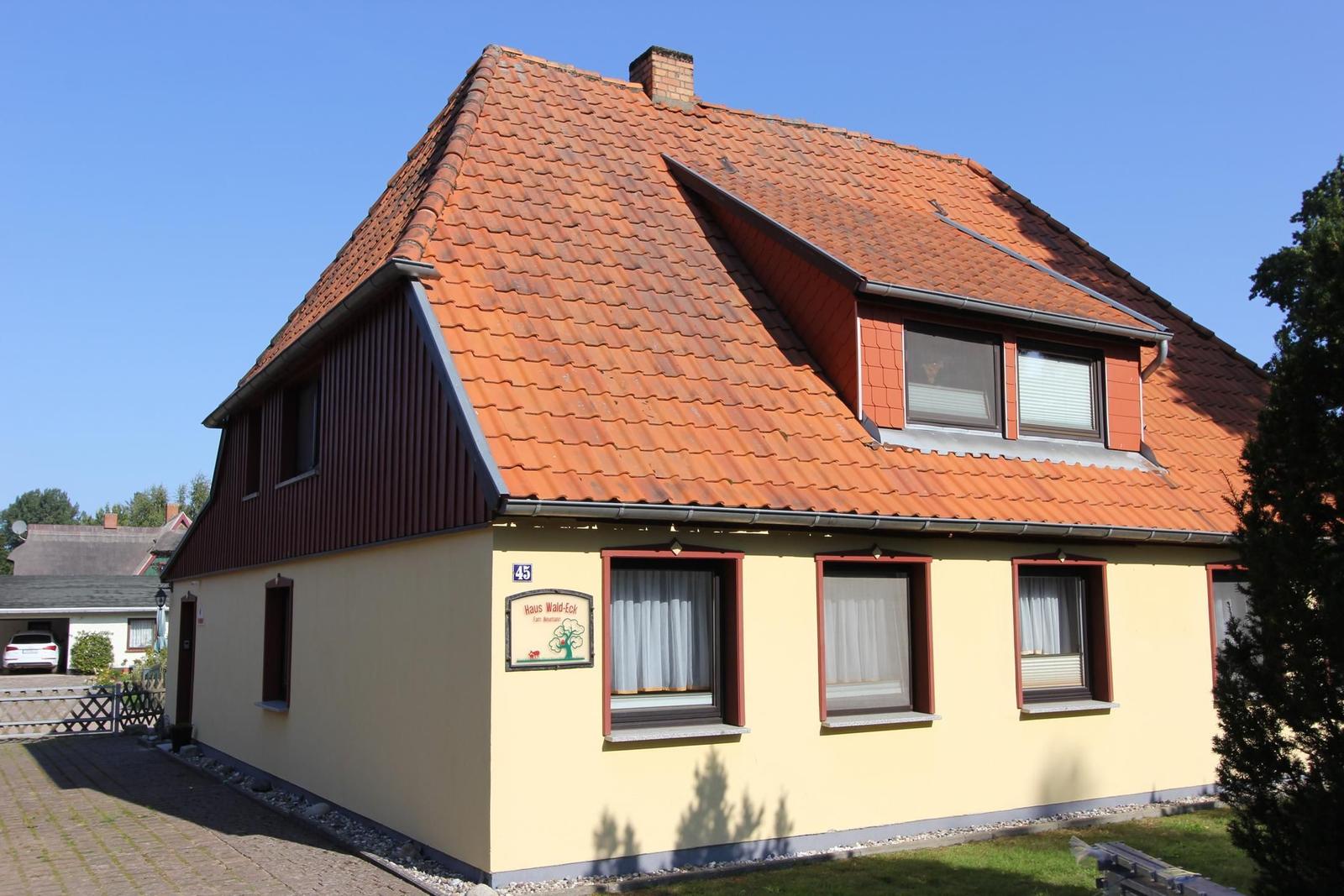 Haus mit gelbem Anstrich, rotem Dach und Fenstern mit weißen Vorhängen.