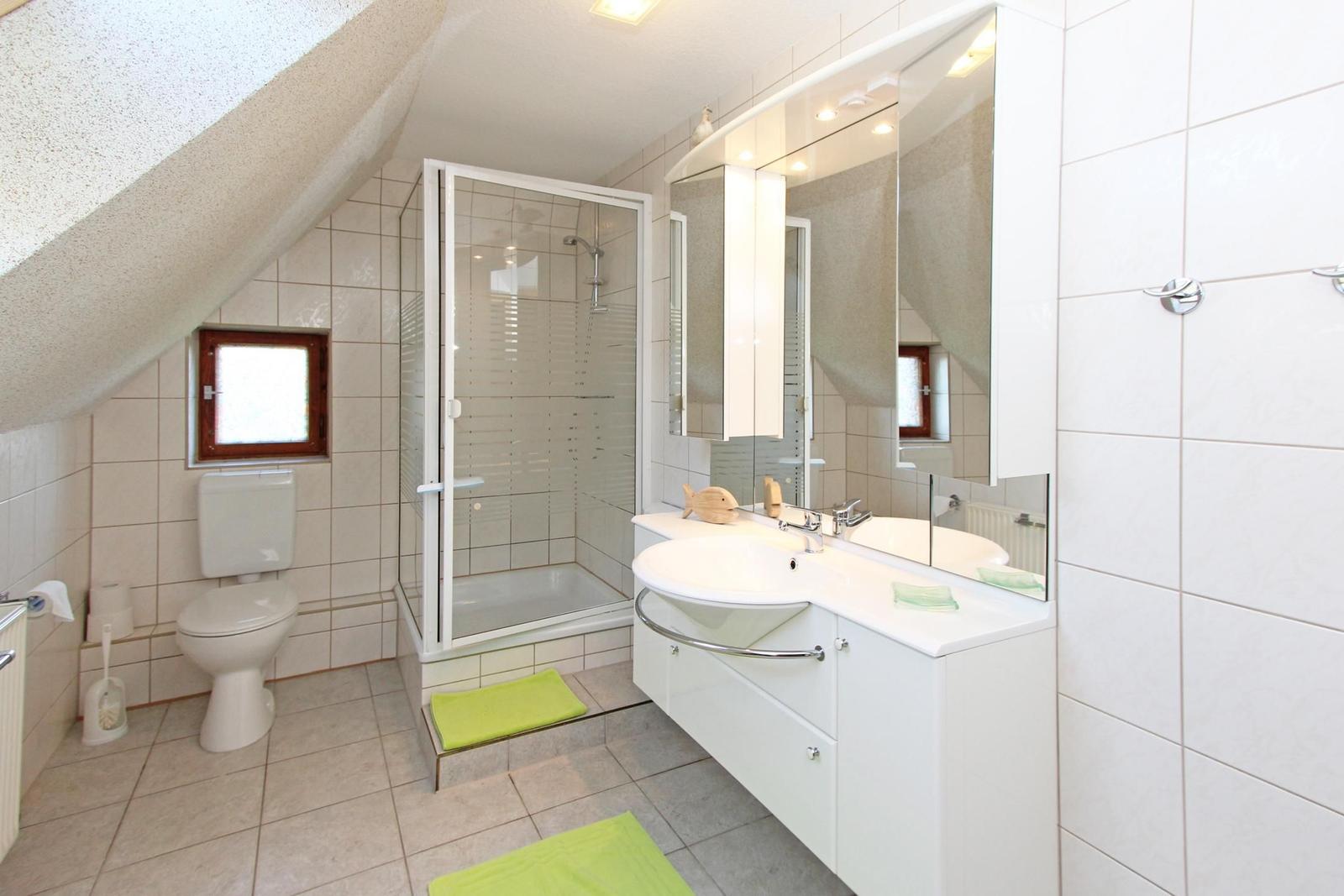 Badezimmer mit Dusche, Waschbecken und Toilette unter Dachschrägen.