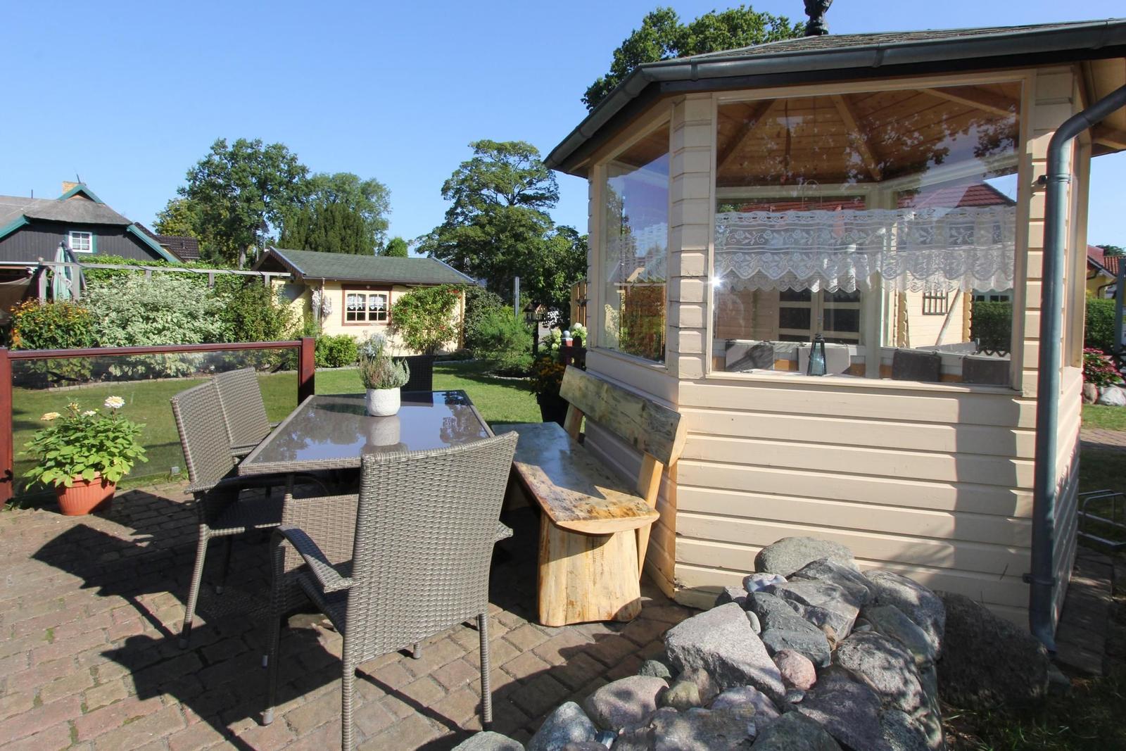 Terrasse mit Tisch, Stühlen und Holzbank neben einem Pavillon mit Glaswänden.