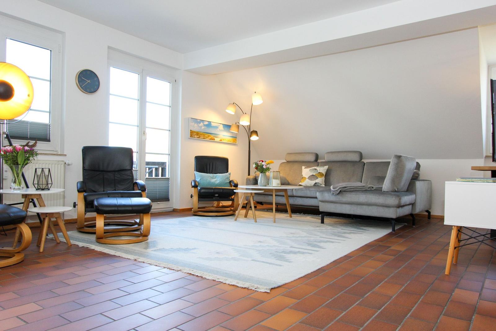 Wohnzimmer mit Sofa, zwei Sesseln, Tisch und Teppich auf Terrakottboden.
