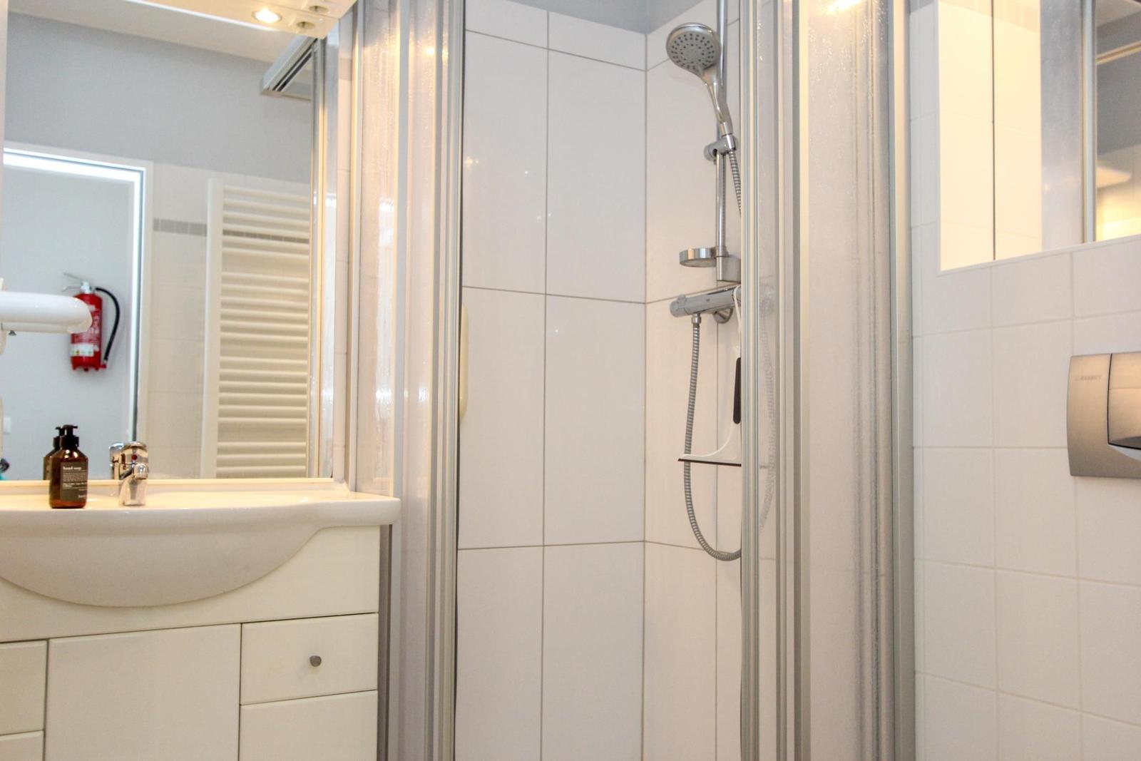 Badezimmer mit Dusche, Waschbecken und Spiegel. Weiße Fliesen und moderne Ausstattung.