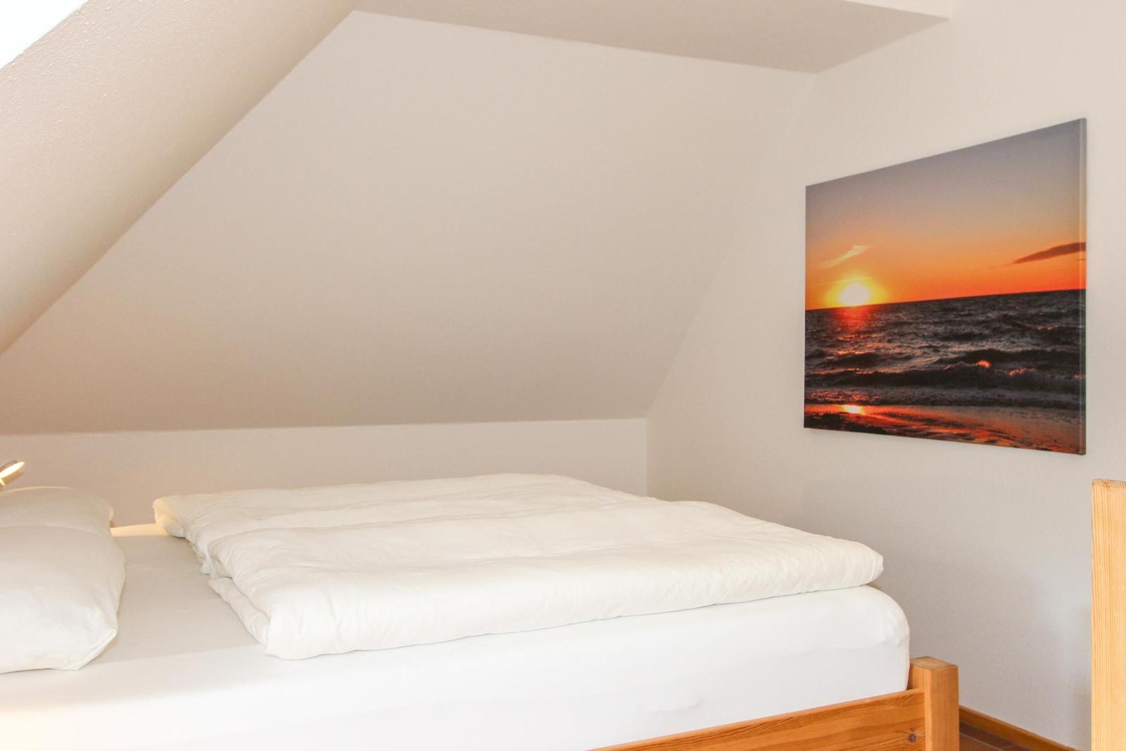 Schlafzimmer mit Dachschräge, Bett und Wandbild mit Sonnenuntergang.