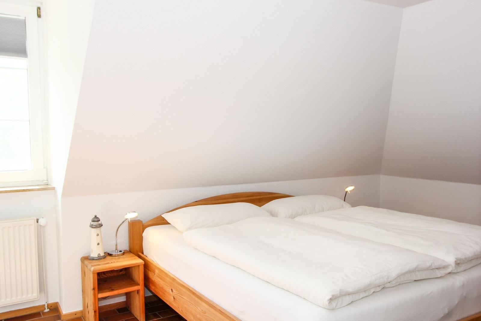 Schlafzimmer mit Doppelbett, Nachttisch und Lampe. Fenster und Heizung sind sichtbar.