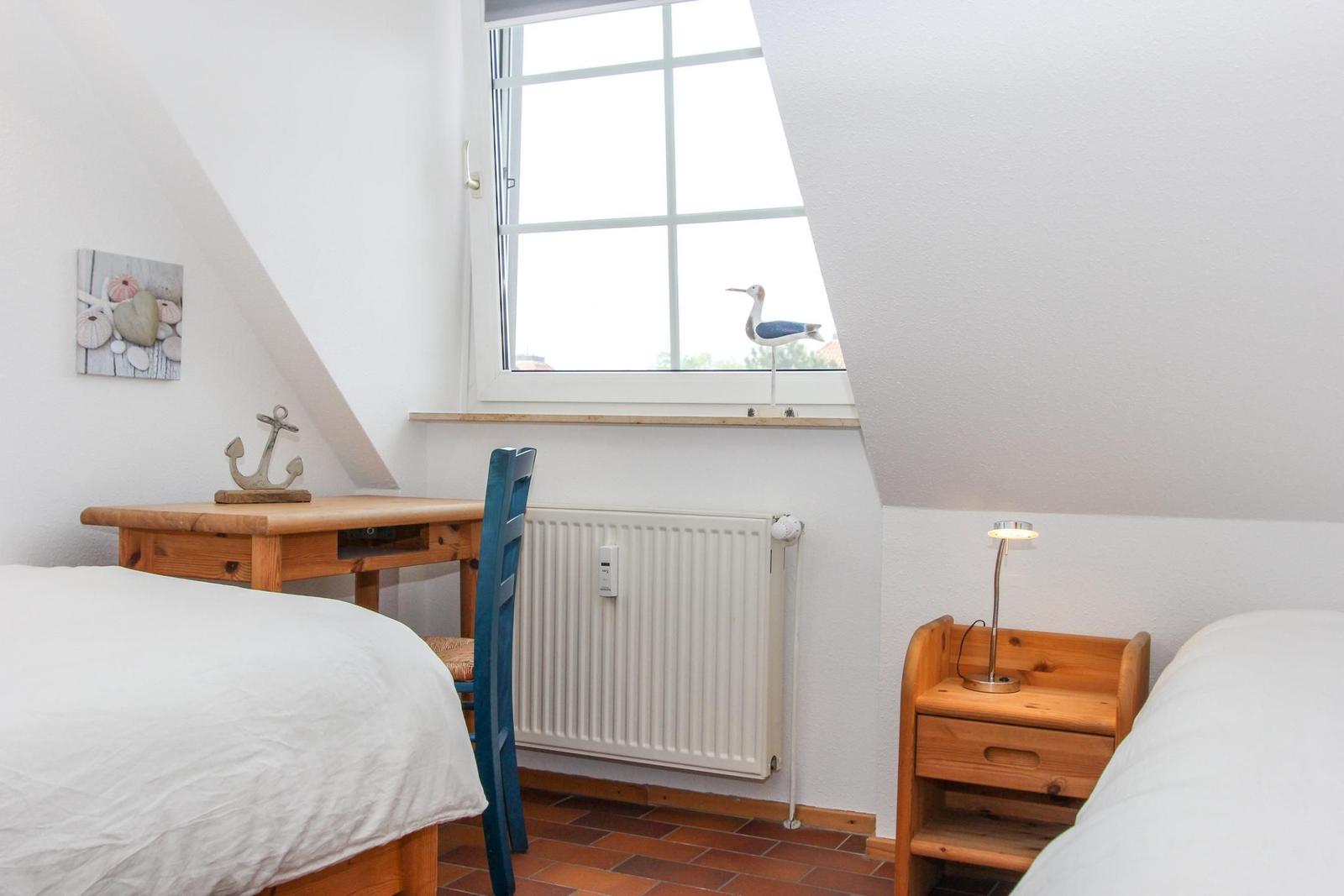 Zimmer mit Dachschrägen, zwei Betten, Holzschreibtisch und Fenster mit Vogeldekoration.