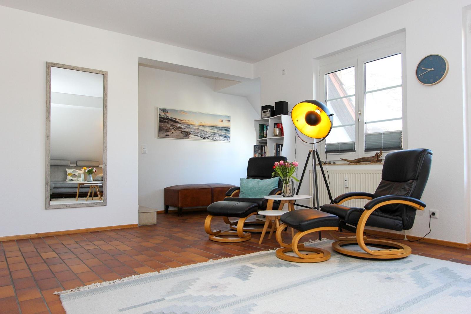 Wohnzimmer mit zwei schwarzen Sesseln, Teppich und Wandspiegel.
