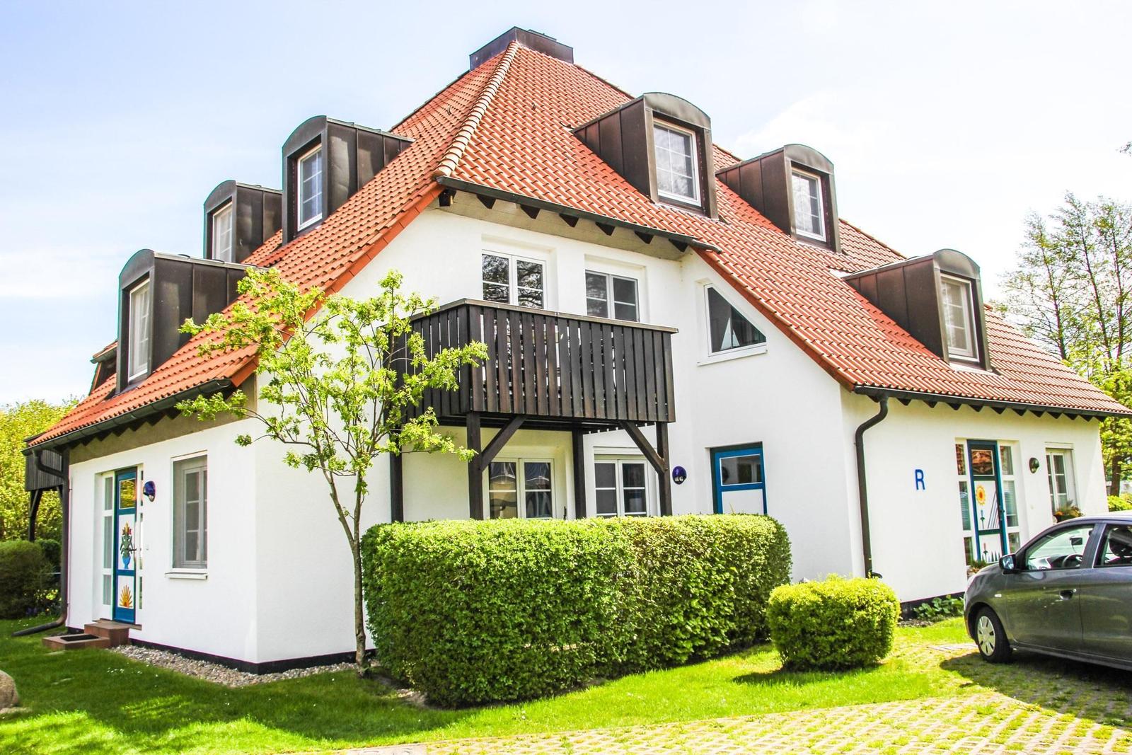 Weiße Villa mit rotem Dach und Balkon. Grün gedeckt und gepflegt.