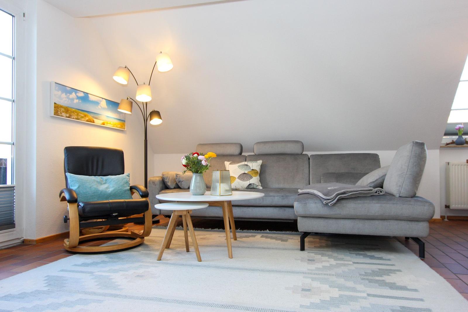 Ein Wohnzimmer mit grauem Sofa, schwarzer Sessel und runden Tischen.