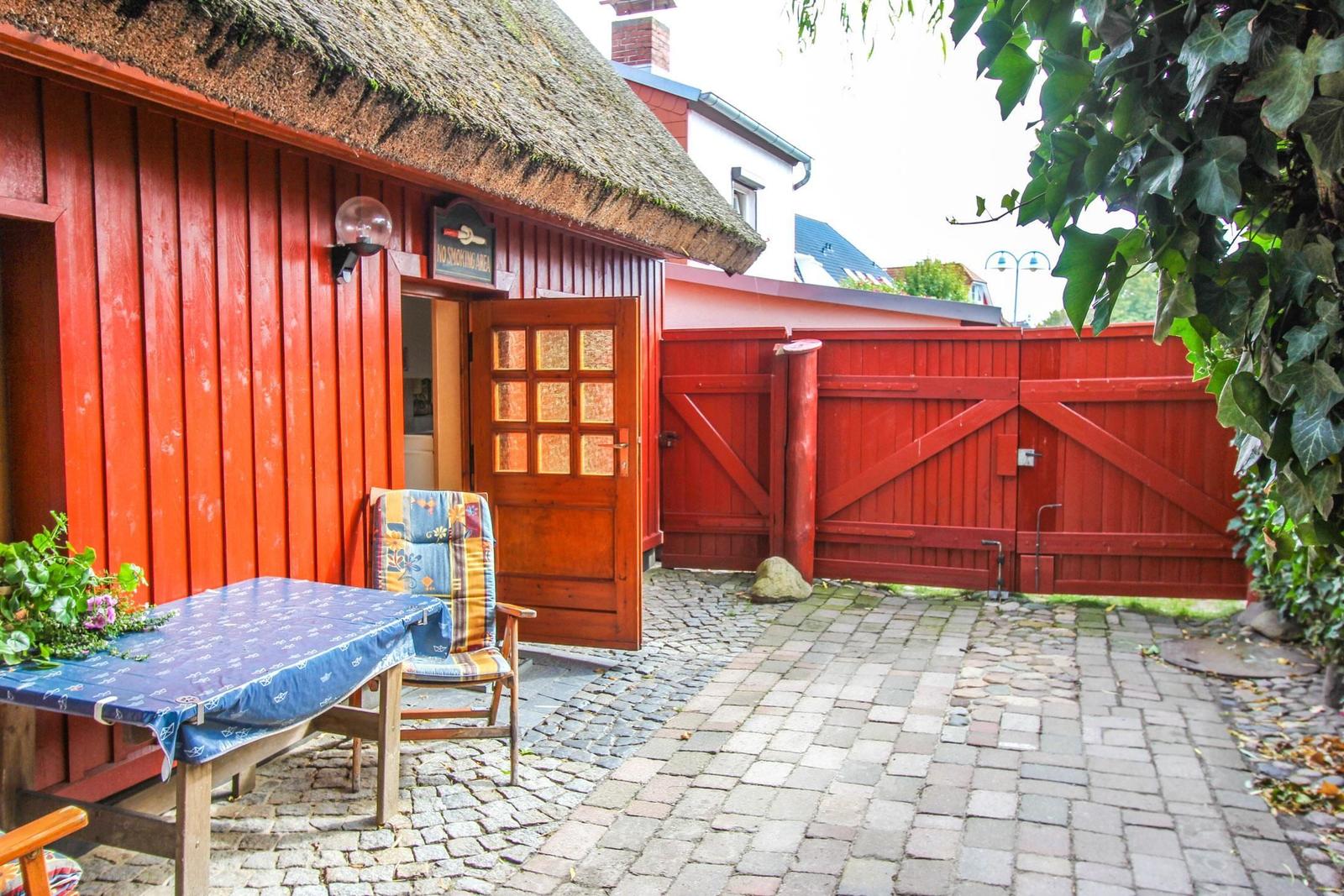 Roter Holzhaus mit Schiebetür, Tisch und Stuhl im Hof mit Steinplatten und rotem Tor.