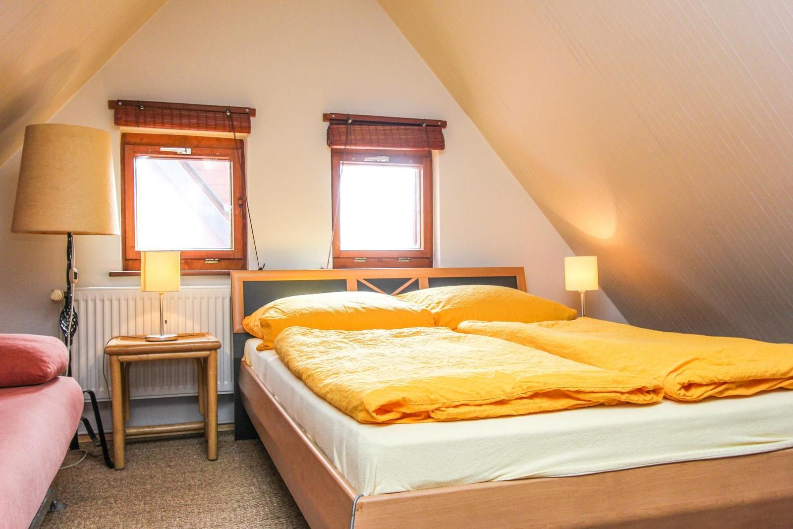 Schlafzimmer mit Doppelbett, zwei Fenstern und Stehlampe.